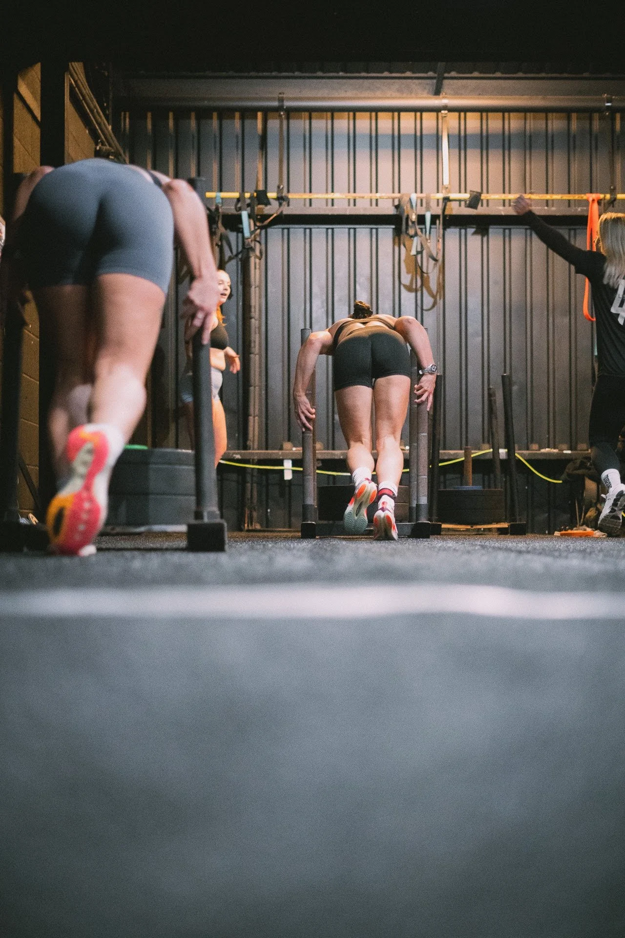 Women participating in a CrossFit workout in a gym, doing push-ups on a low platform with others engaged in different exercises nearby.