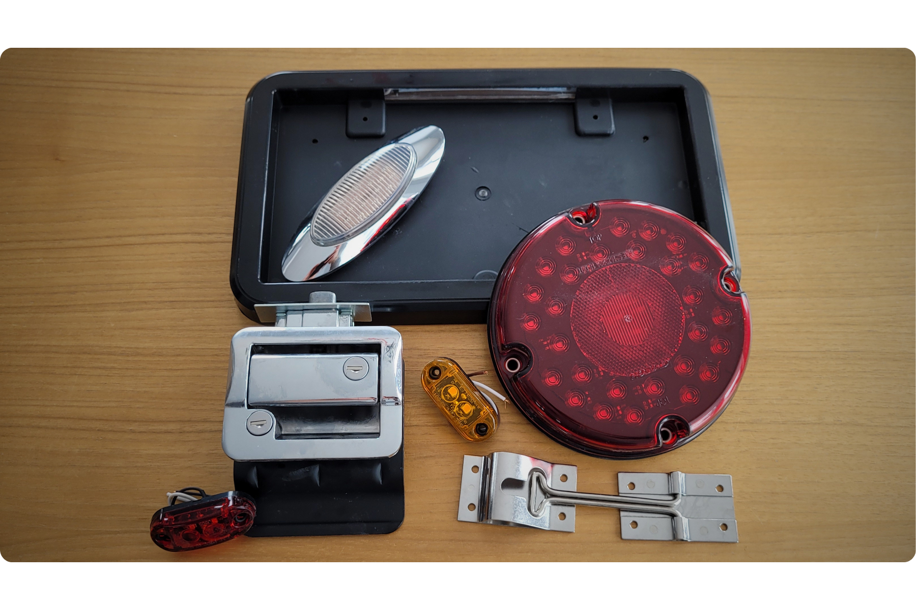 Différents feux arrière de vélo et accessoires, y compris des réflecteurs rouges, un clignotant orange, une bande électrique, et un support en métal, disposés sur une table en bois.