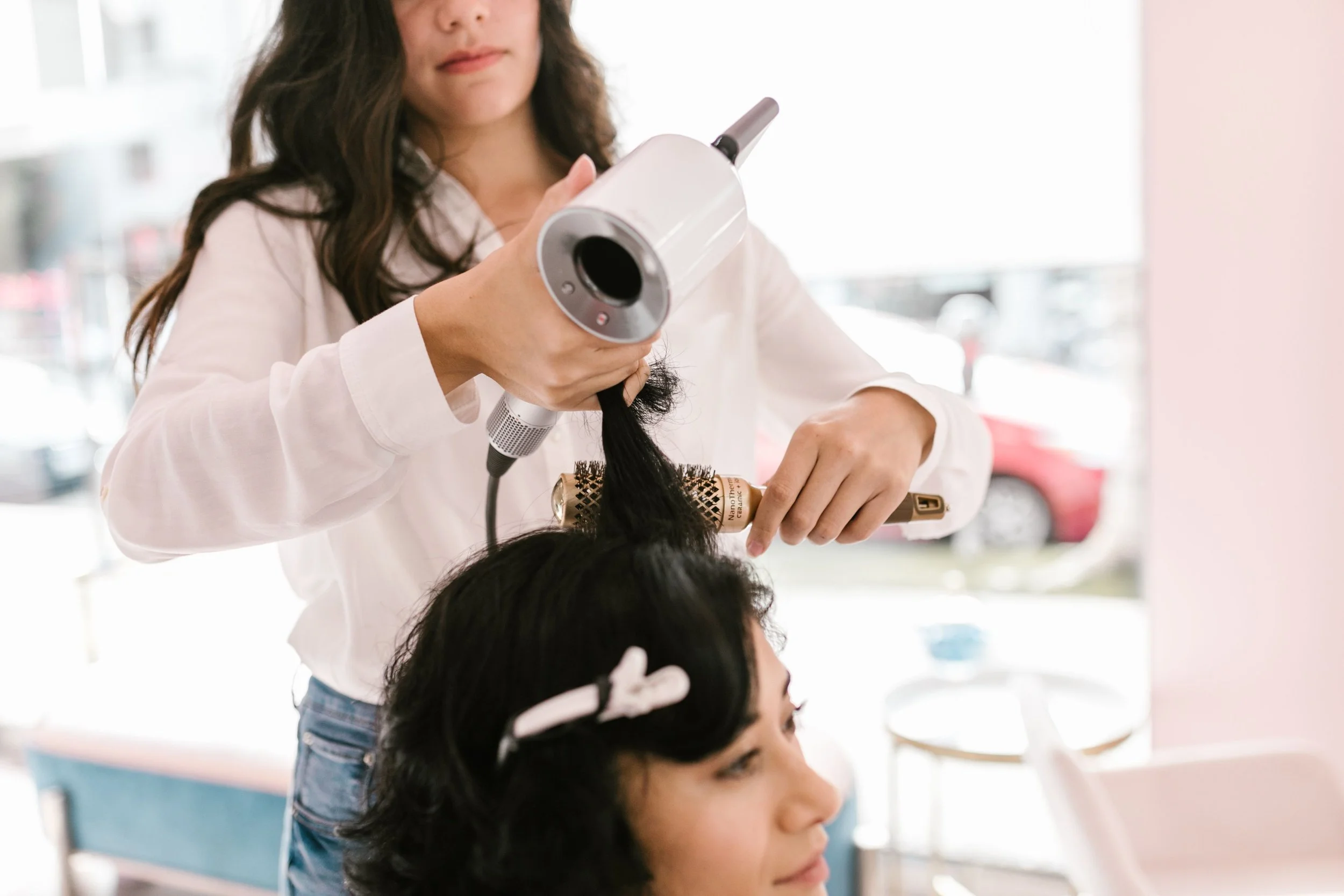 A woman giving another woman a blow dry using a hairdryer and round brush.