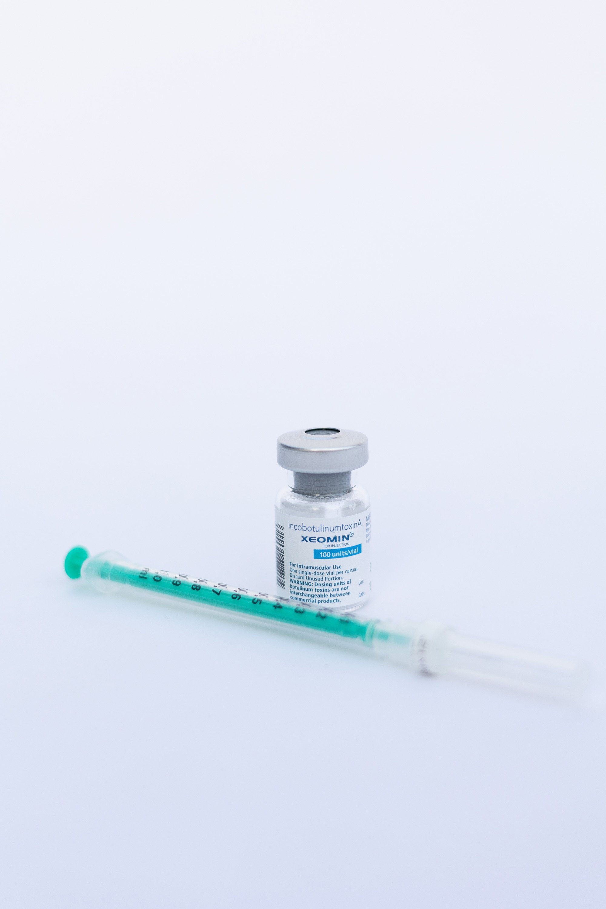 A vial and a medical syringe on a white background, with the syringe positioned horizontally in front of the vial.