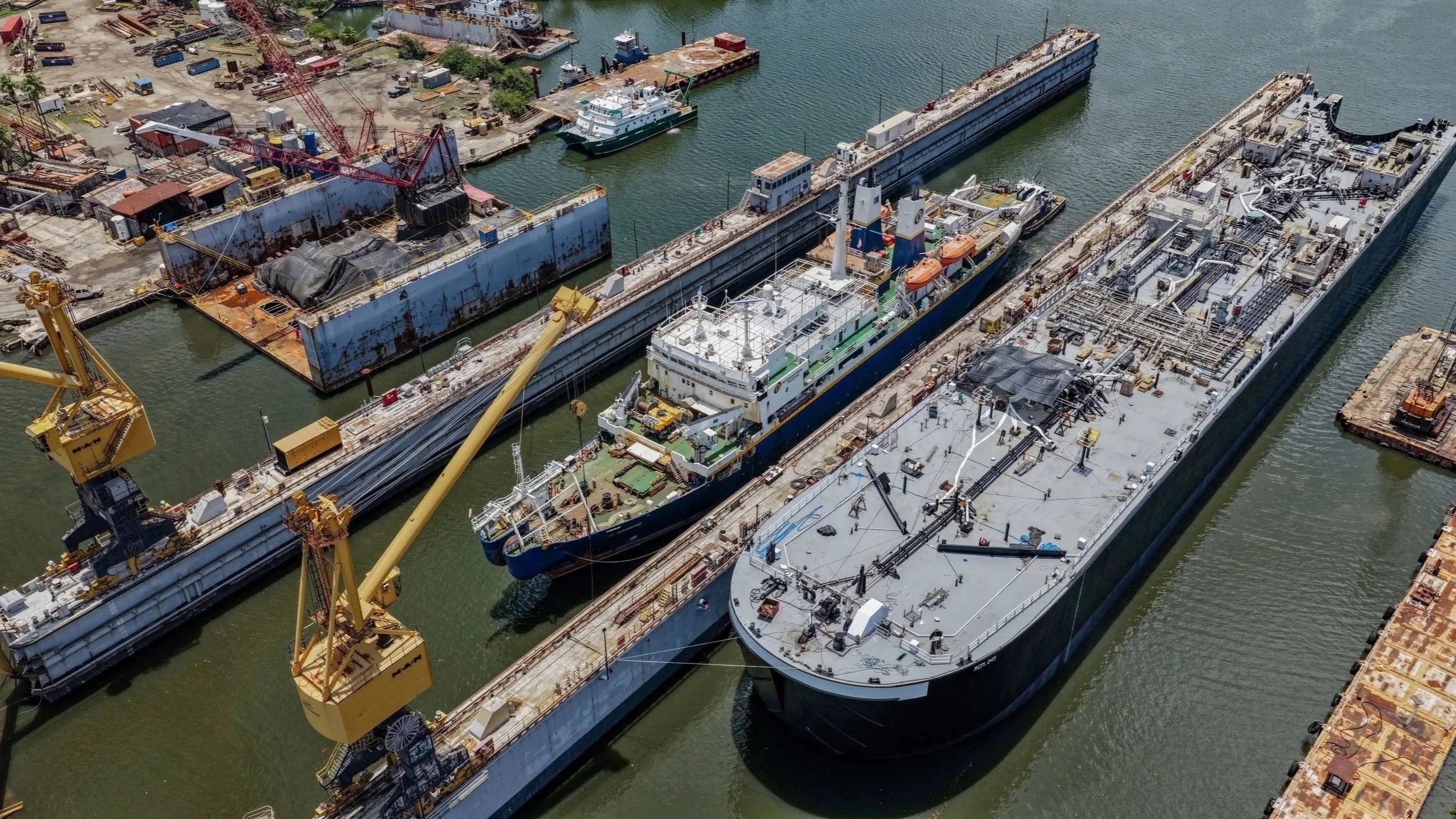 An aerial view of a shipyard with multiple ships under construction, surrounded by cranes, scaffolding, and industrial equipment.