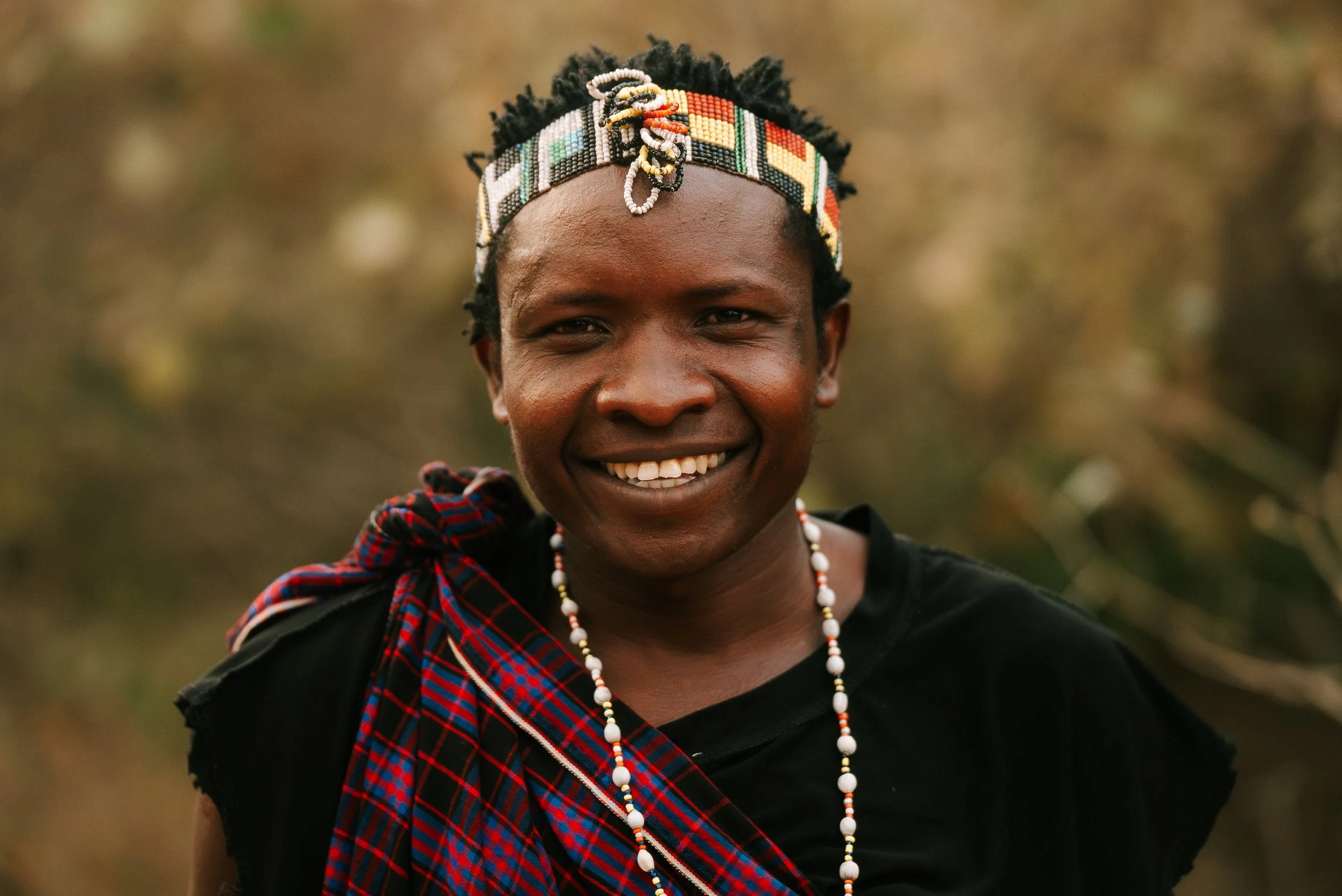A woman from Kenya wearing traditional Maasai jewelry and attire, smiling outdoors.