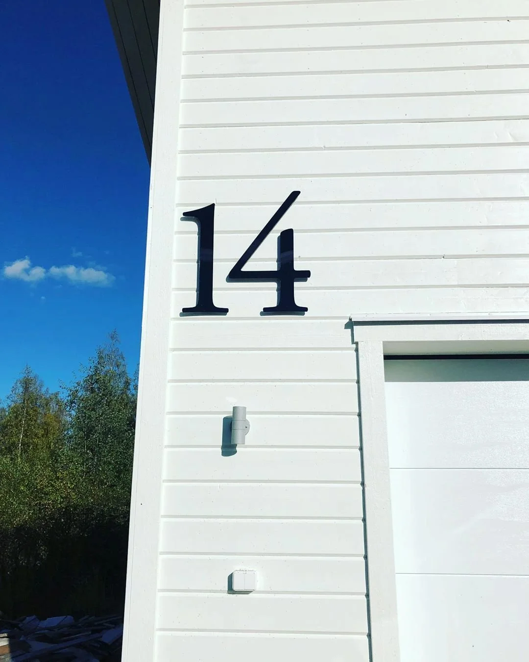 Husnummer 14 i mørkegrå akryl på lys væg ved garage