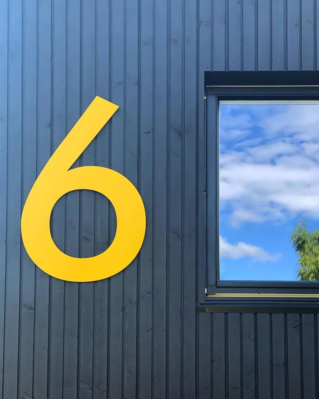 Husnummer 6 i gul akryl/stål på mørkegrå væg ved hoveddør