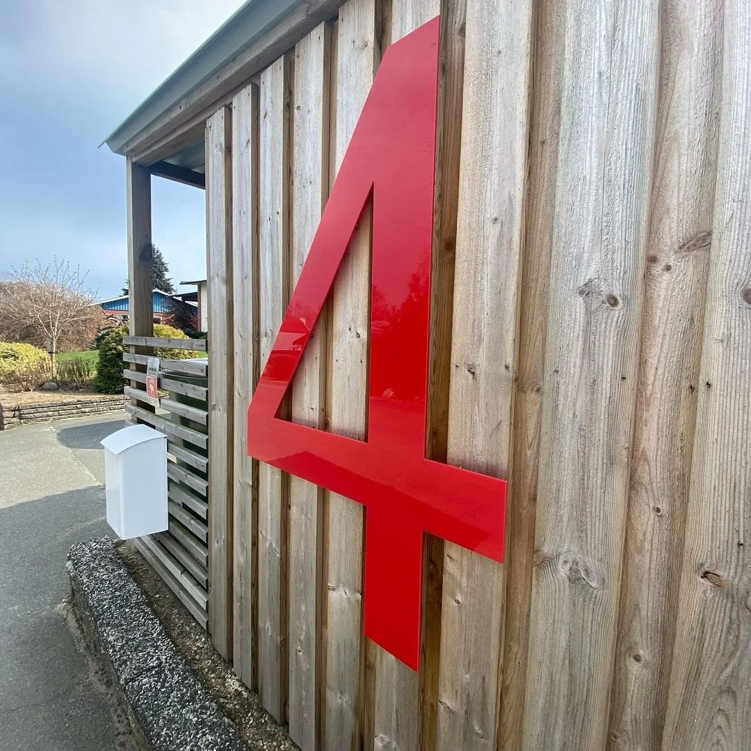 Husnummer 4 i rød akryl på grå ubehandlet træfacade