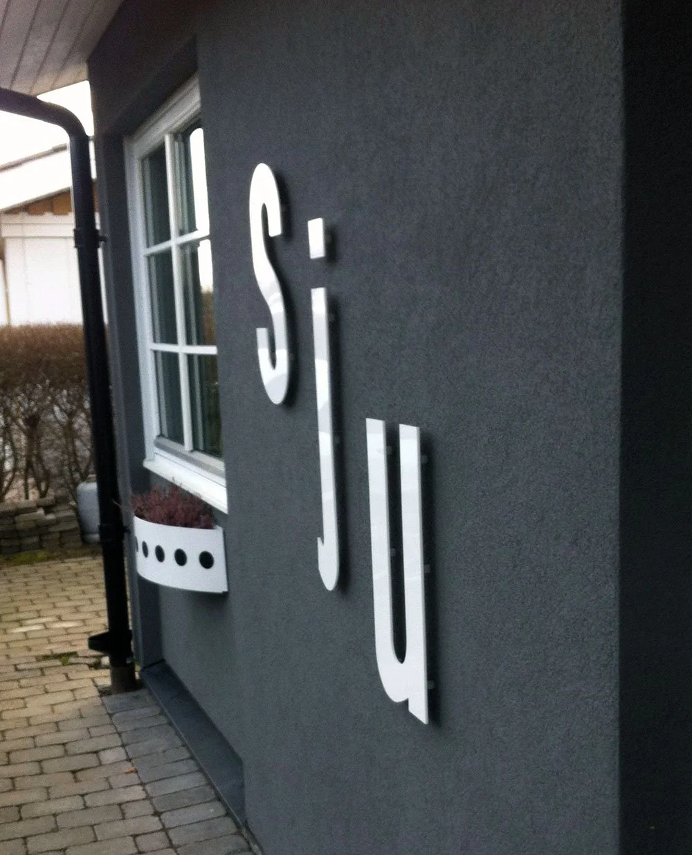 Facadetekst 'sju' i hvid stål med vindue på sort facade – kreativ adressemarkering