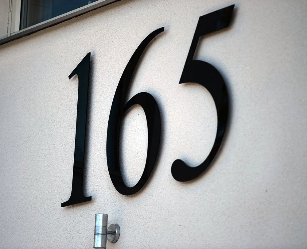 Husnummer 165 i sort stål på hvid glittet facade – tydelig og moderne
