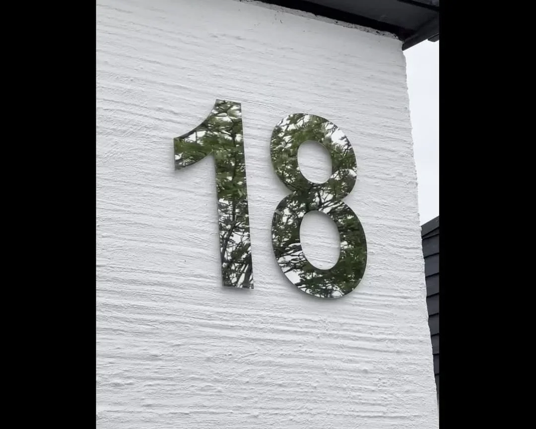 Husnummer 18 i spejlpoleret rustfrit stål på hvit naturstensfacade