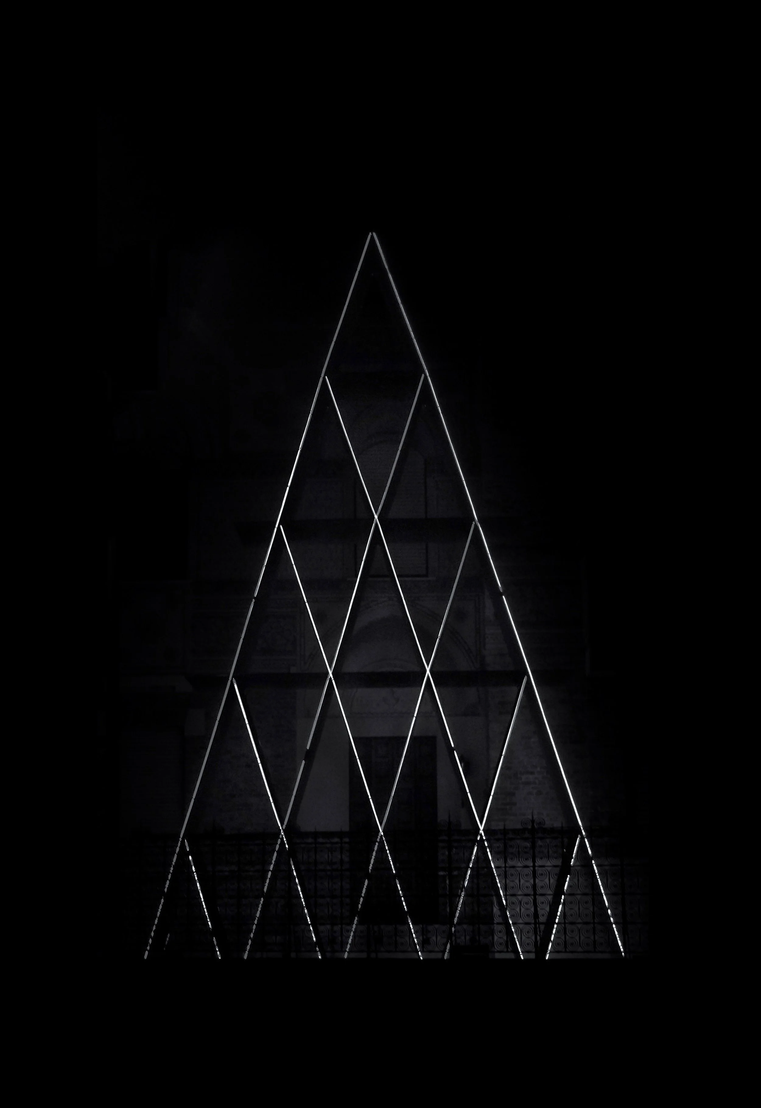 Struttura di luci a forma di piramide tridimensionale creata con linee luminose in un ambiente buio.