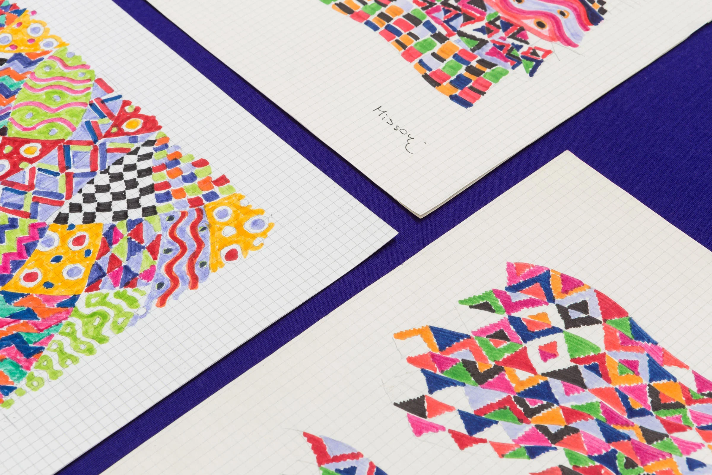 Disegni colorati su fogli di carta con sfondo a quadretti, firmati con il nome 'Missoni'.