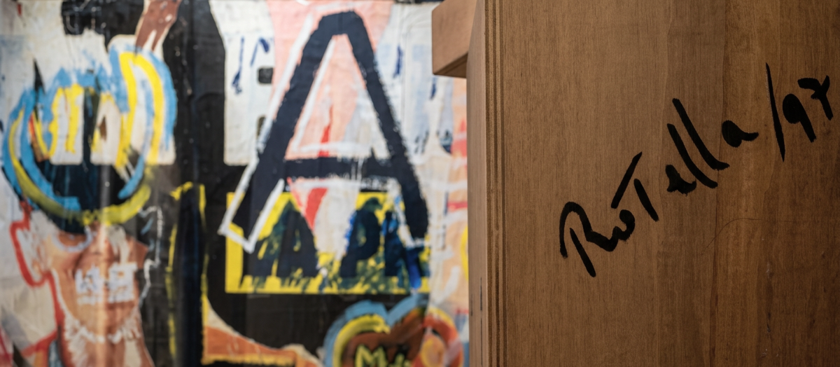 Immagine di un muro con graffiti colorato e firma in penna su legno.