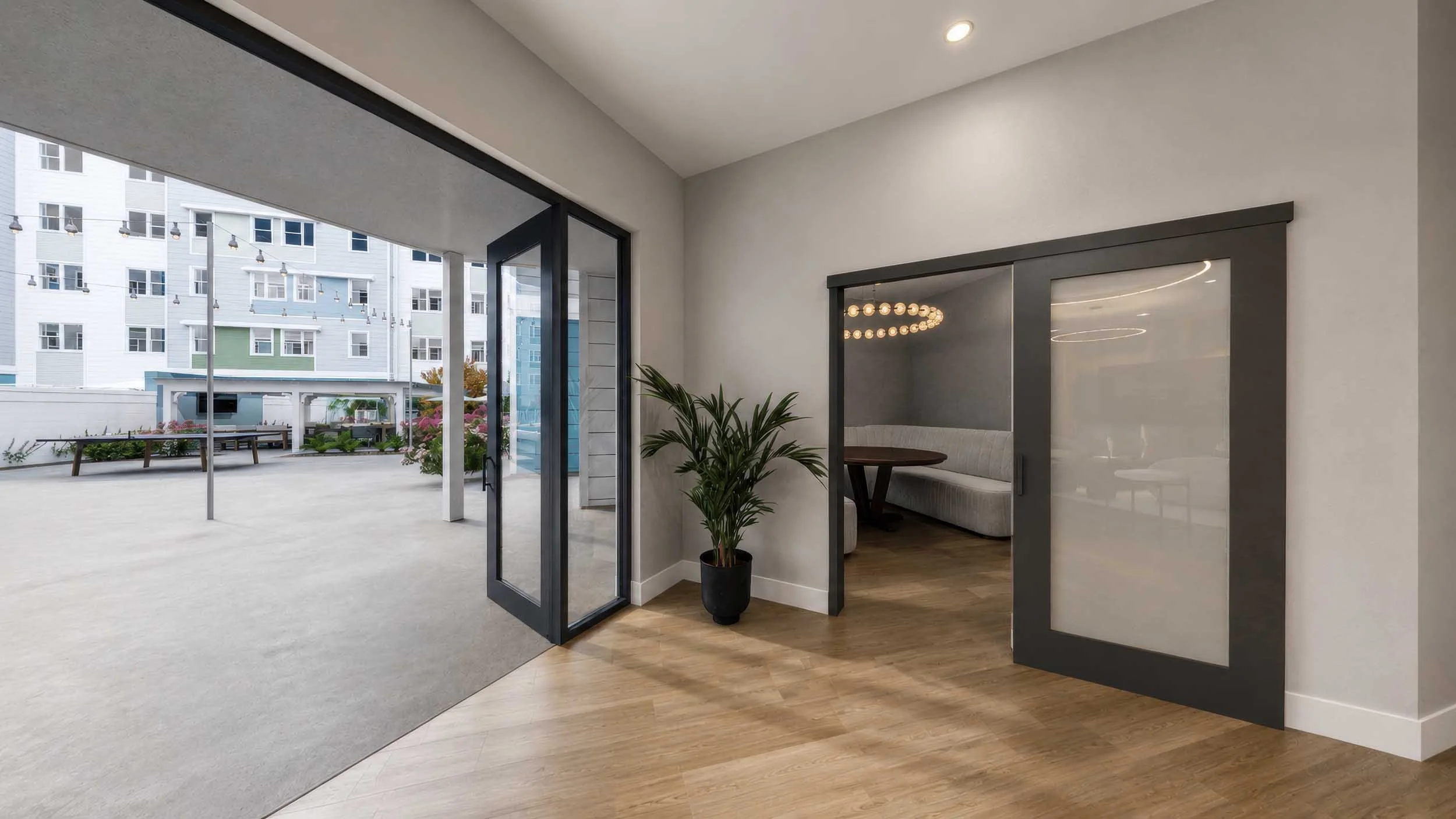 Modern indoor space with large glass doors opening to an outdoor patio, a plant in a pot, and a cozy booth seating area with a round table inside.