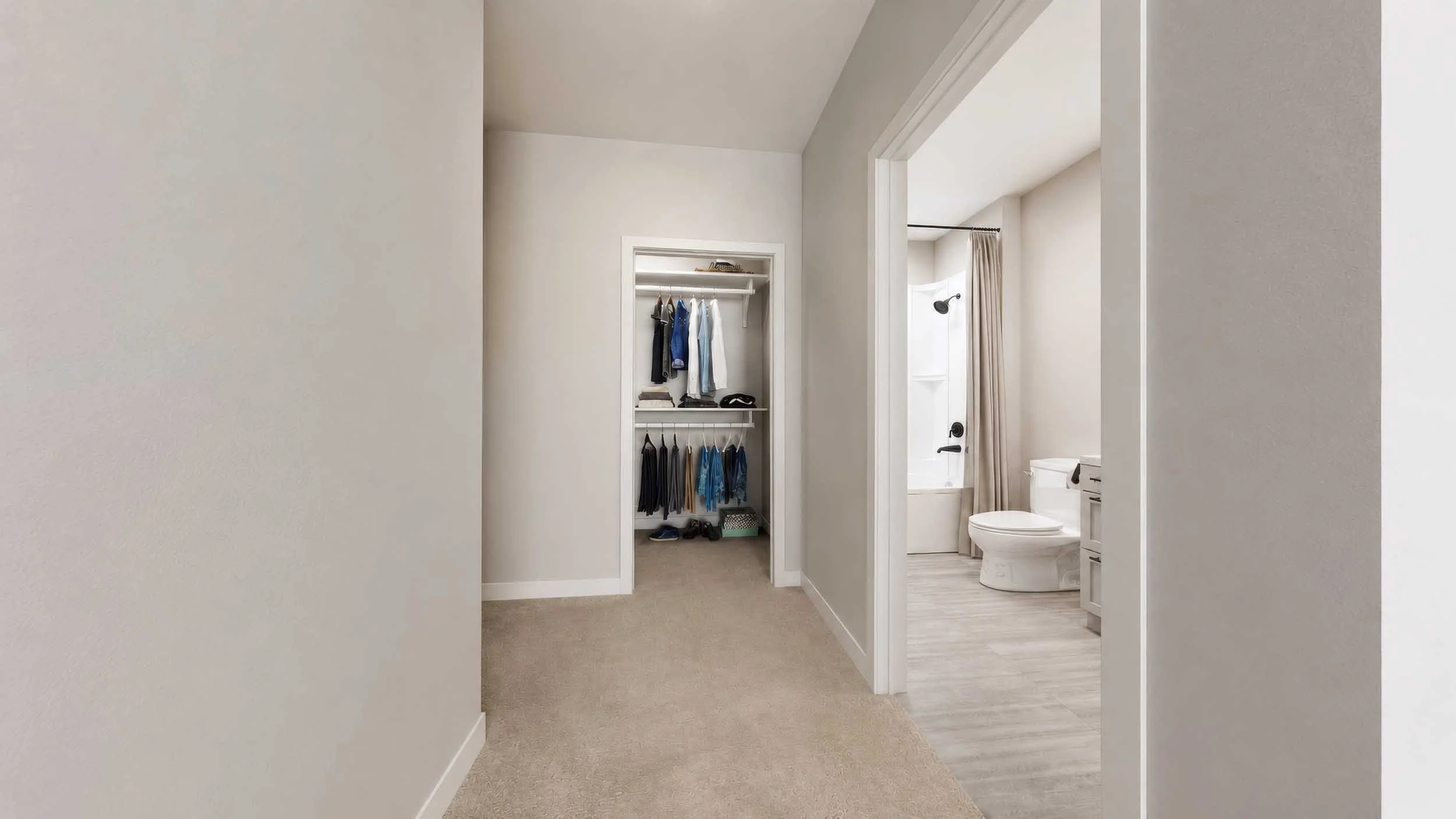 A view into a house's walk-in closet and bathroom with beige carpet, a white toilet, and a partial view of a bathtub with shower curtain, with a doorway separating the spaces.