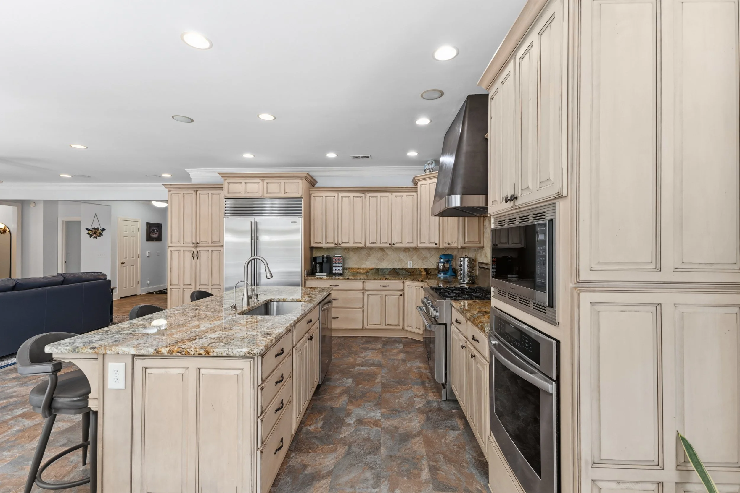 Kitchen with beige cabinets, granite countertops, stainless steel appliances including double oven and refrigerator, and a kitchen island with a sink.