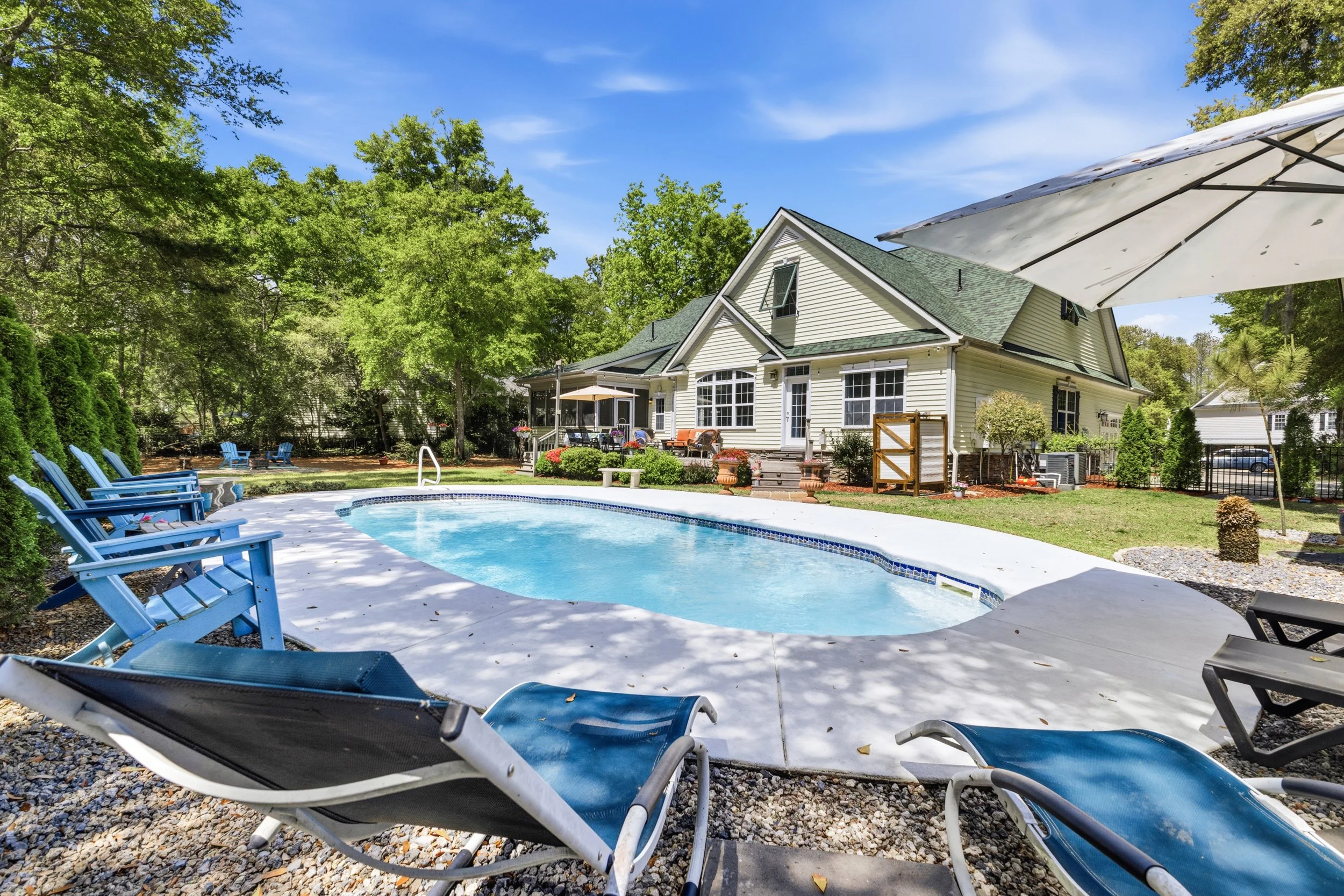 A backyard with a kidney-shaped swimming pool, surrounded by trees and lounge chairs, with a house in the background.