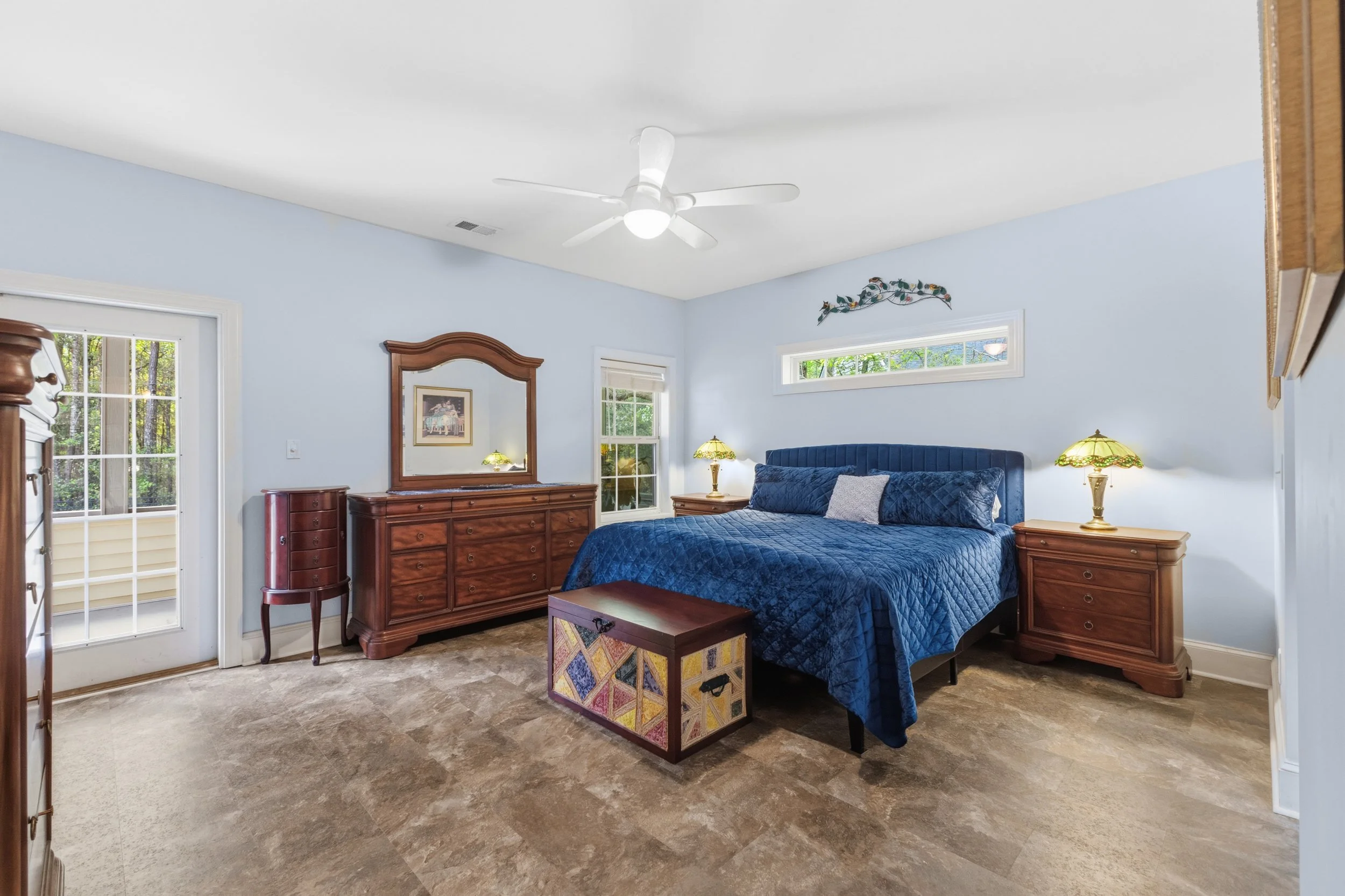 Bedroom with light blue walls, wooden furniture, a bed with blue bedding, and a ceiling fan.