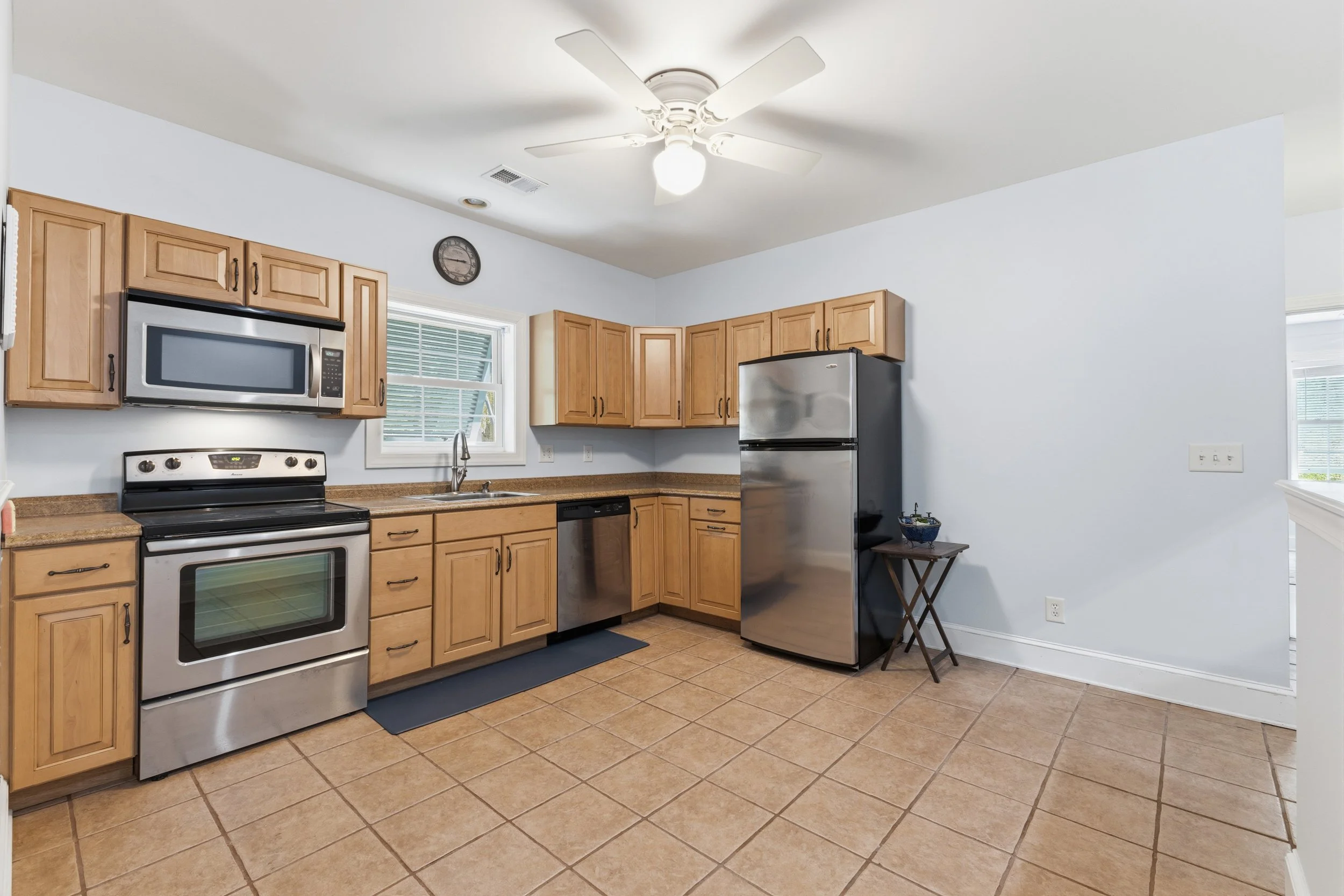 Kitchen with wooden cabinets, stainless steel appliances, a window above the sink, a ceiling fan, and beige tiled floor.