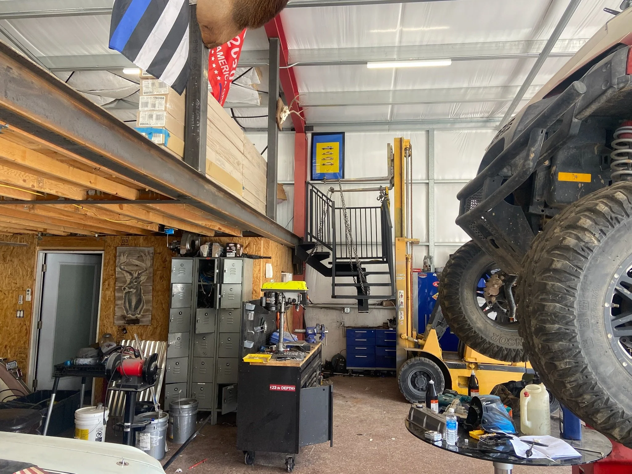 View of a cluttered garage or workshop with tools, lockers, a workbench, a vehicle lift, an off-road vehicle, and various equipment and supplies.