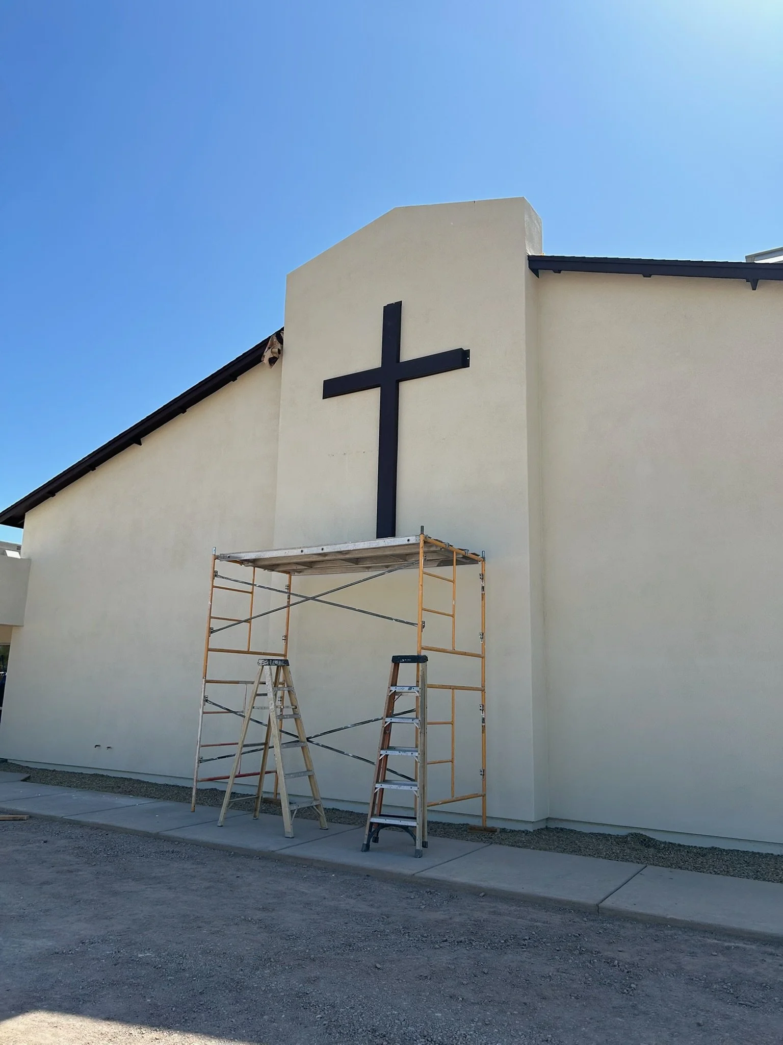 Construction scaffolding in front of a church wall with a large black cross.