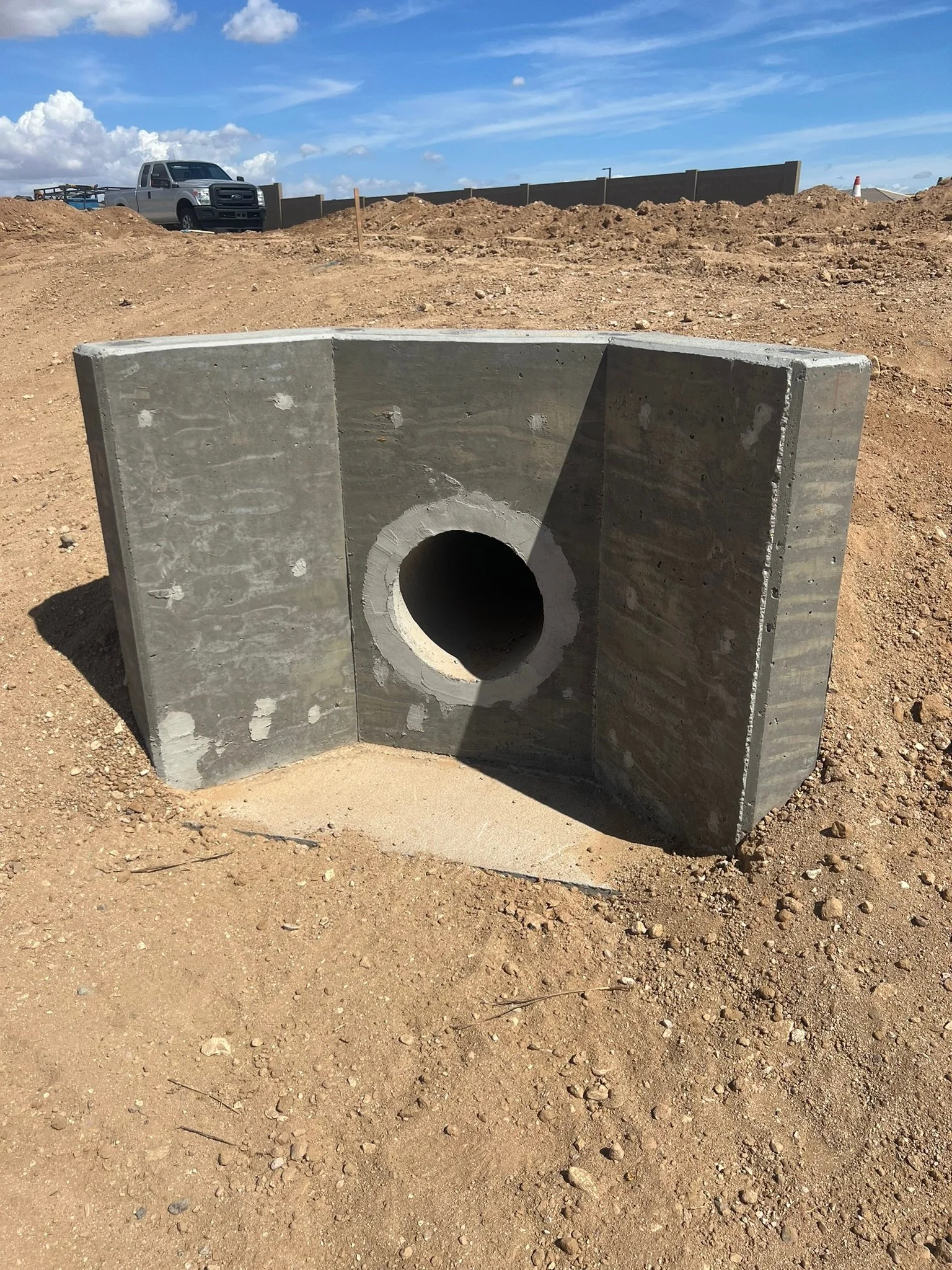 Concrete culvert pipe fitting at a construction site with dirt and a vehicle in the background.