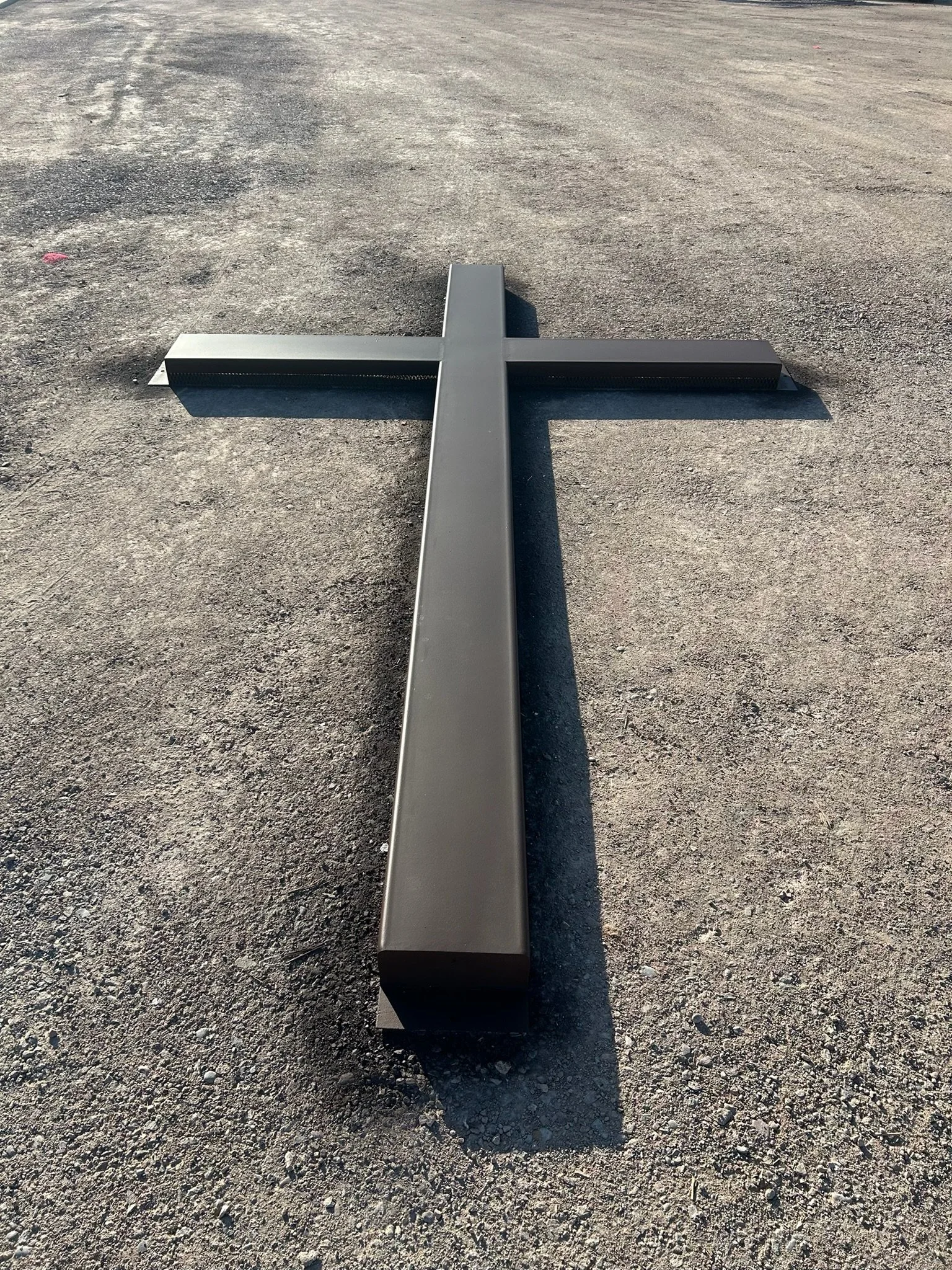 A large, black cross lying flat on a gravel surface outdoors