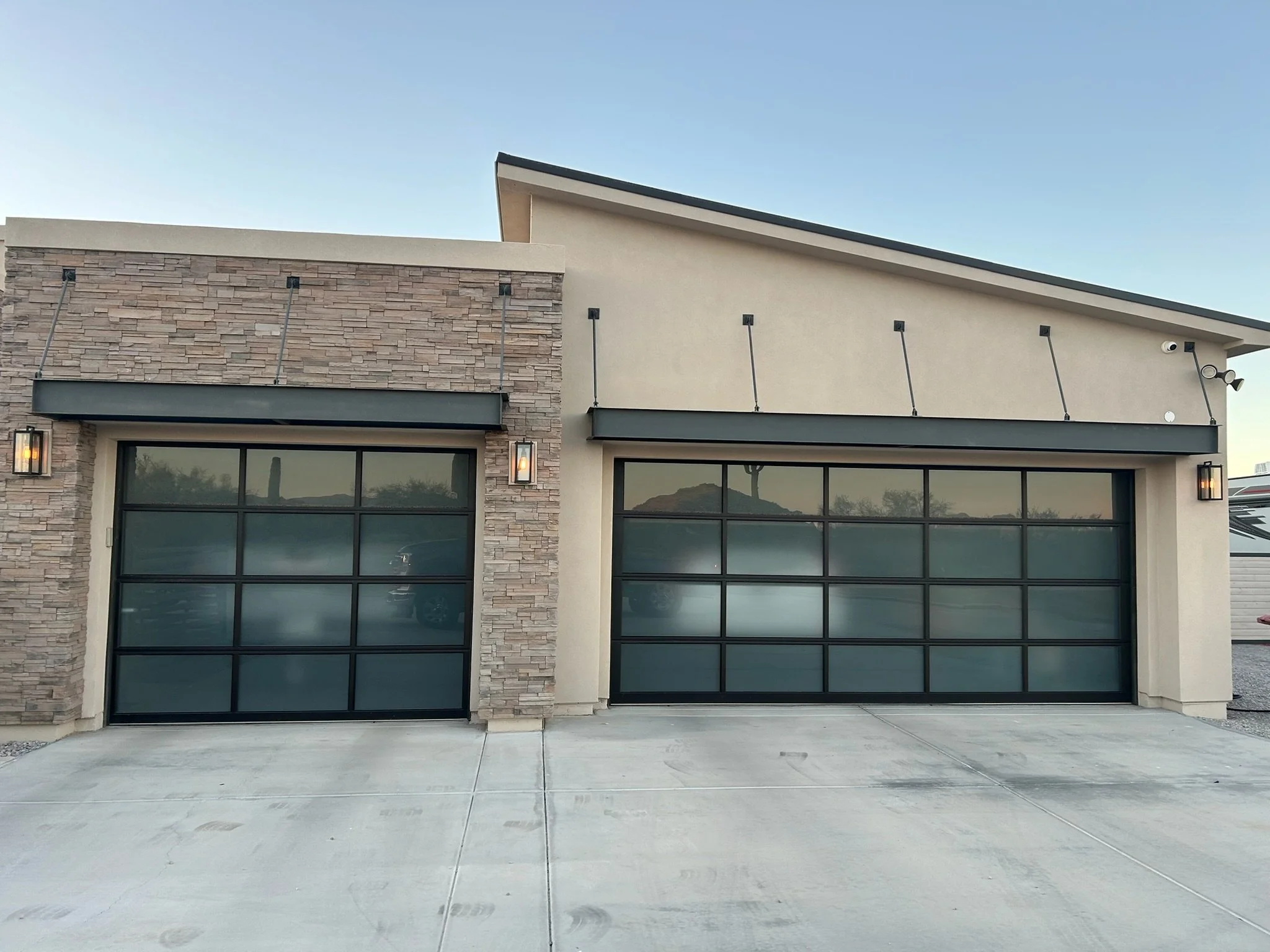 Front view of a modern house with two black garage doors, stone and stucco exterior, and exterior lighting fixtures.