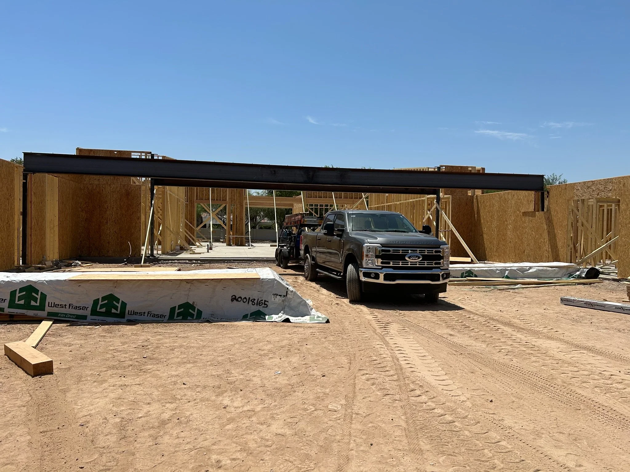 Construction site with wooden framing, a Ford truck, and construction materials on dirt ground under a blue sky.