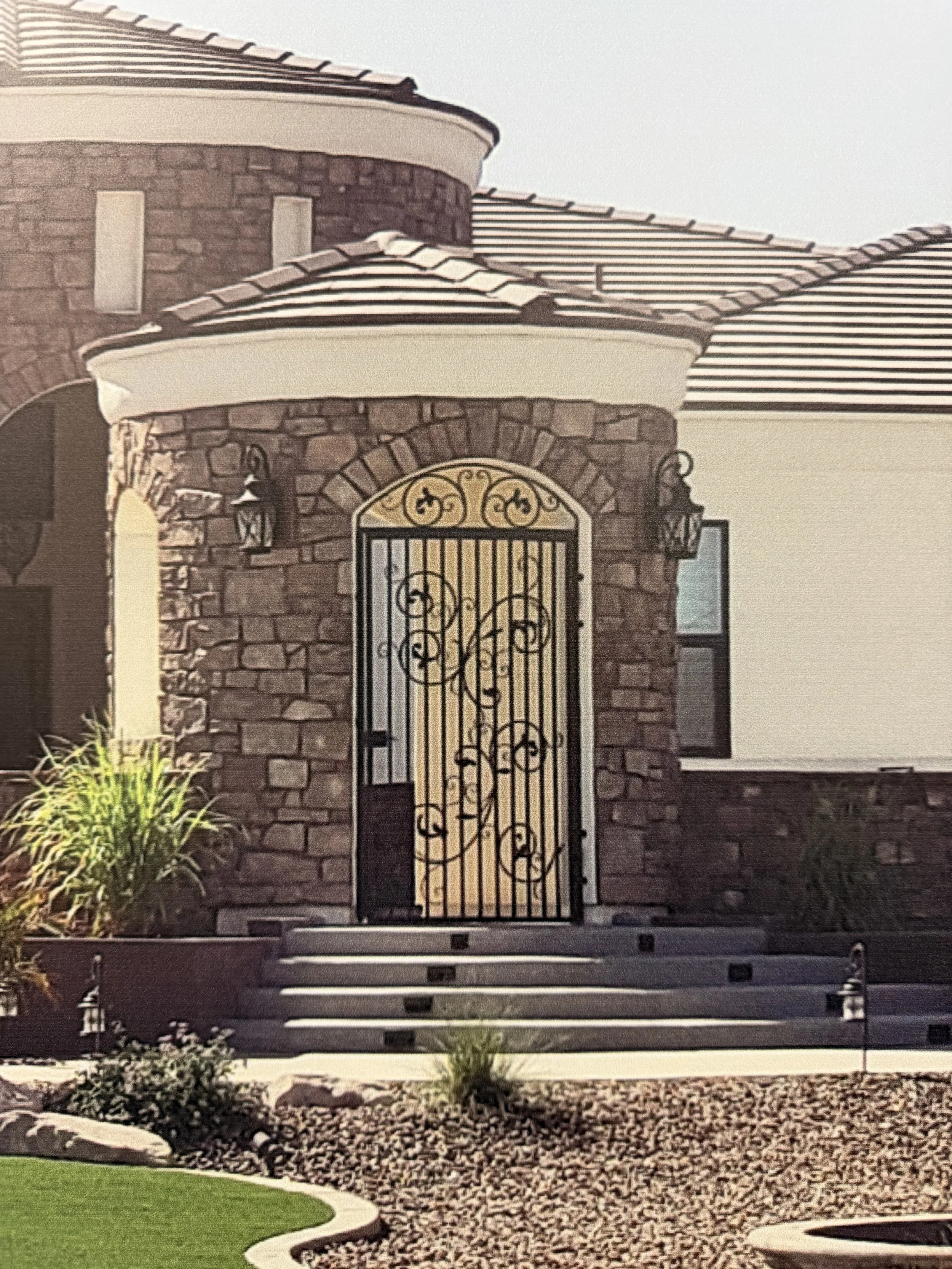 Front door of a house with a decorative wrought iron gate, brick exterior, stone steps, and landscaped yard.