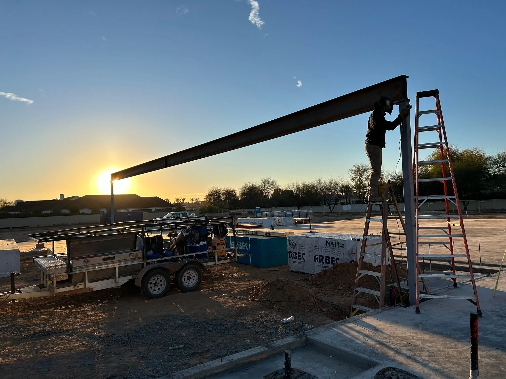 Construction worker on a ladder installing a steel beam at a construction site during sunset.