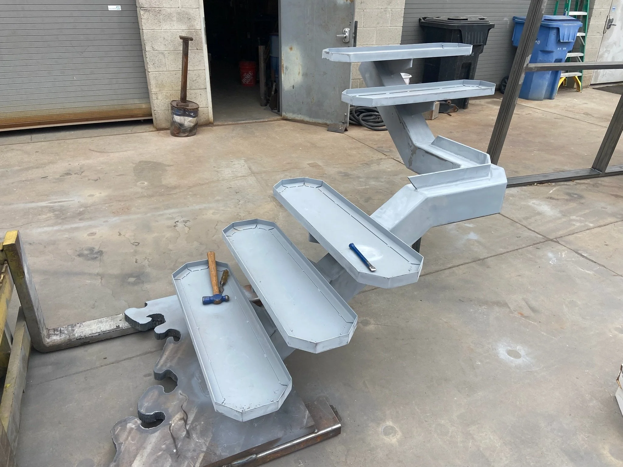 Metal staircase in construction with four steps, tools resting on the steps, in a garage or workshop.