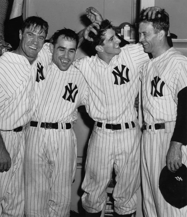Four men in New York Yankees baseball uniforms smiling and celebrating together.
