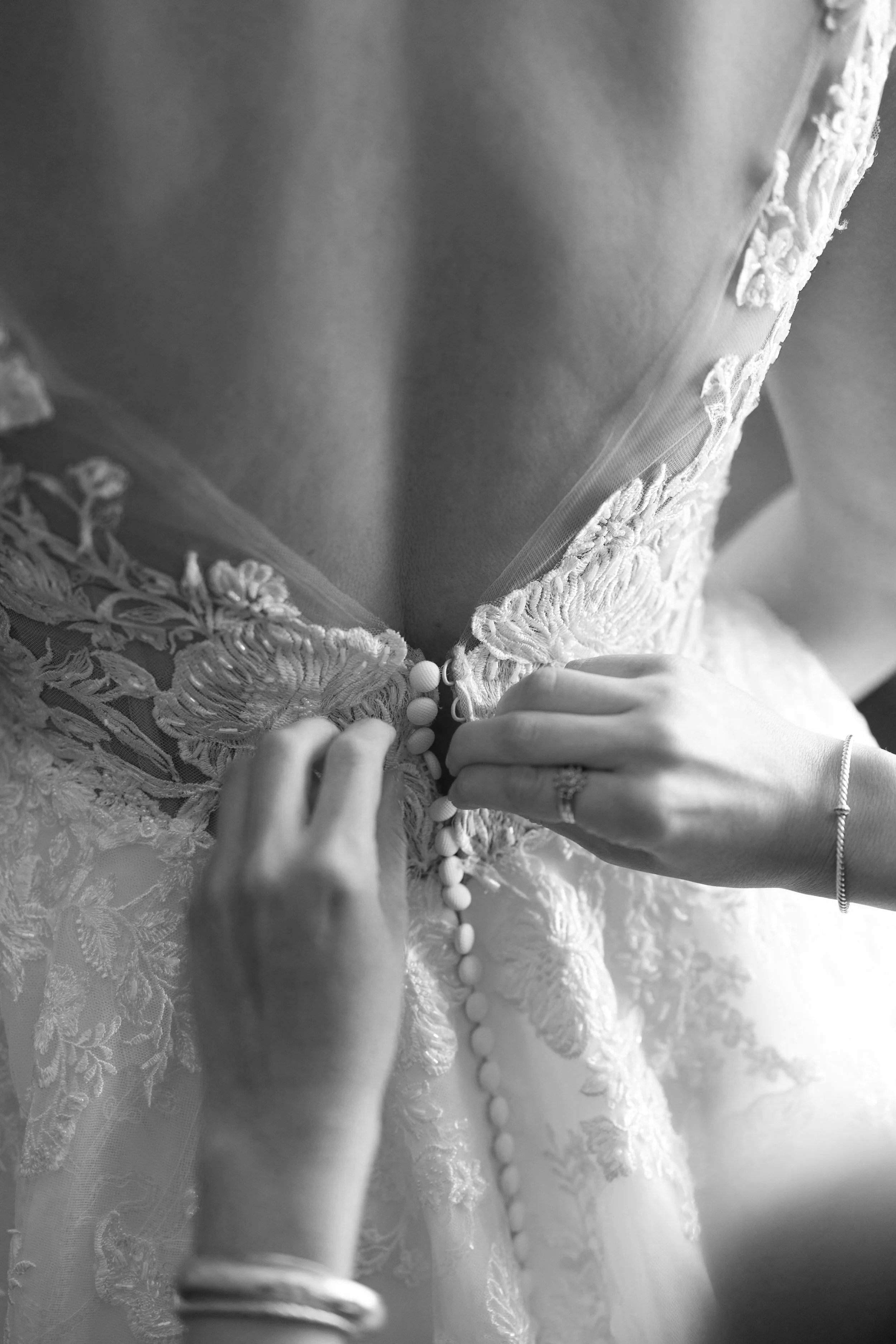 Close-up of a person fastening buttons on the back of a wedding dress with lace and embroidery details.