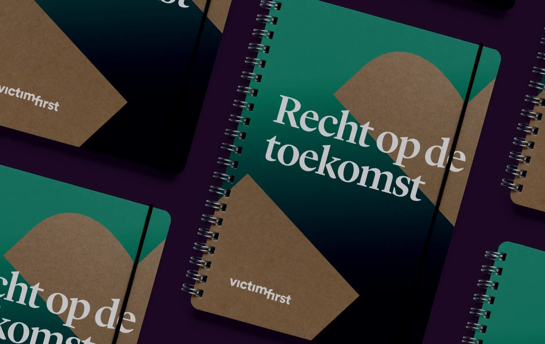 Several spiral-bound notebooks from VictimFirst with the words 'Recht op de toekomst' on the covers, arranged on a dark surface. BigStoryShort client.