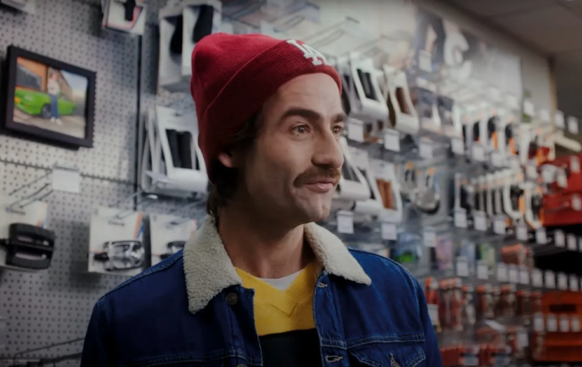 A man wearing a red beanie, a yellow and black striped shirt, and a denim jacket with a shearling collar, standing in a UNION bike store aisle with various gadgets and accessories on the shelves behind him. BigStoryShort client.