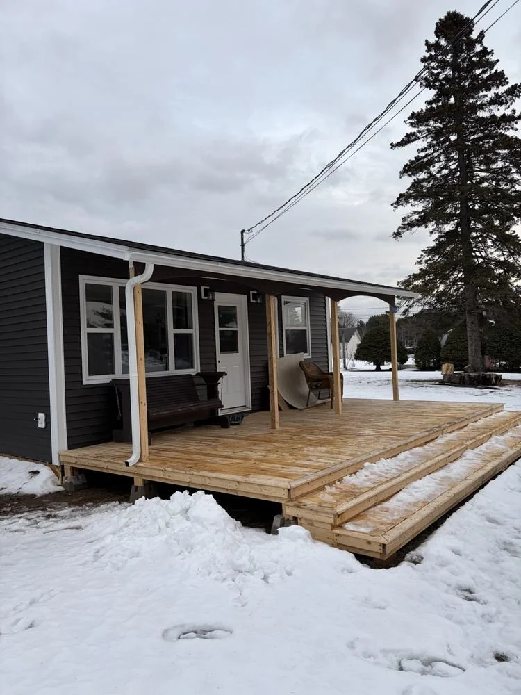 Newly built wooden deck attached to a house with snow on the ground and a large tree in the background.
