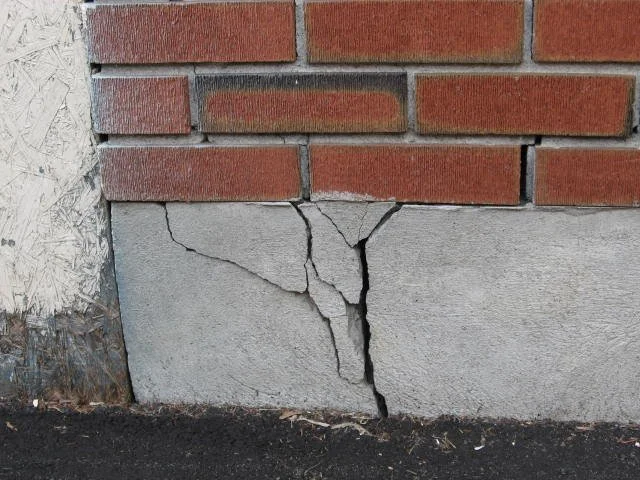 Cracked concrete foundation below brick wall on exterior building
