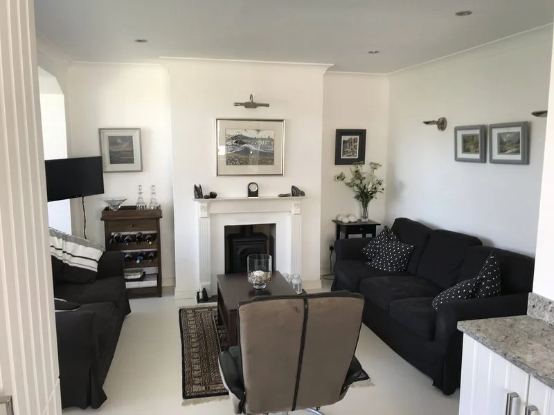 Living room with a white fireplace, black sofas, a TV, picture frames, a vase with flowers, and a coffee table.