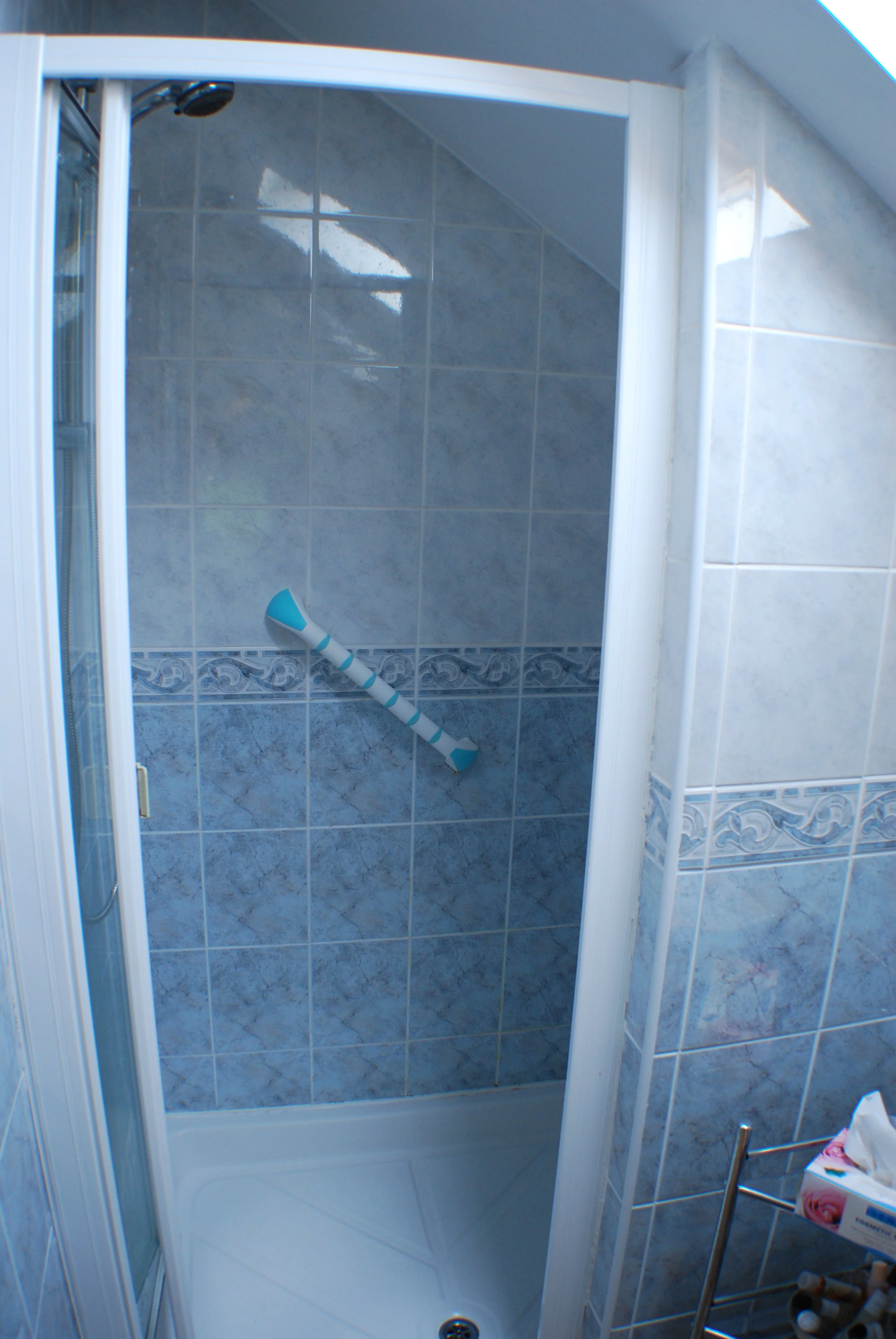 Inside a shower with gray marble tiles, a handheld showerhead, and a white shower tray.