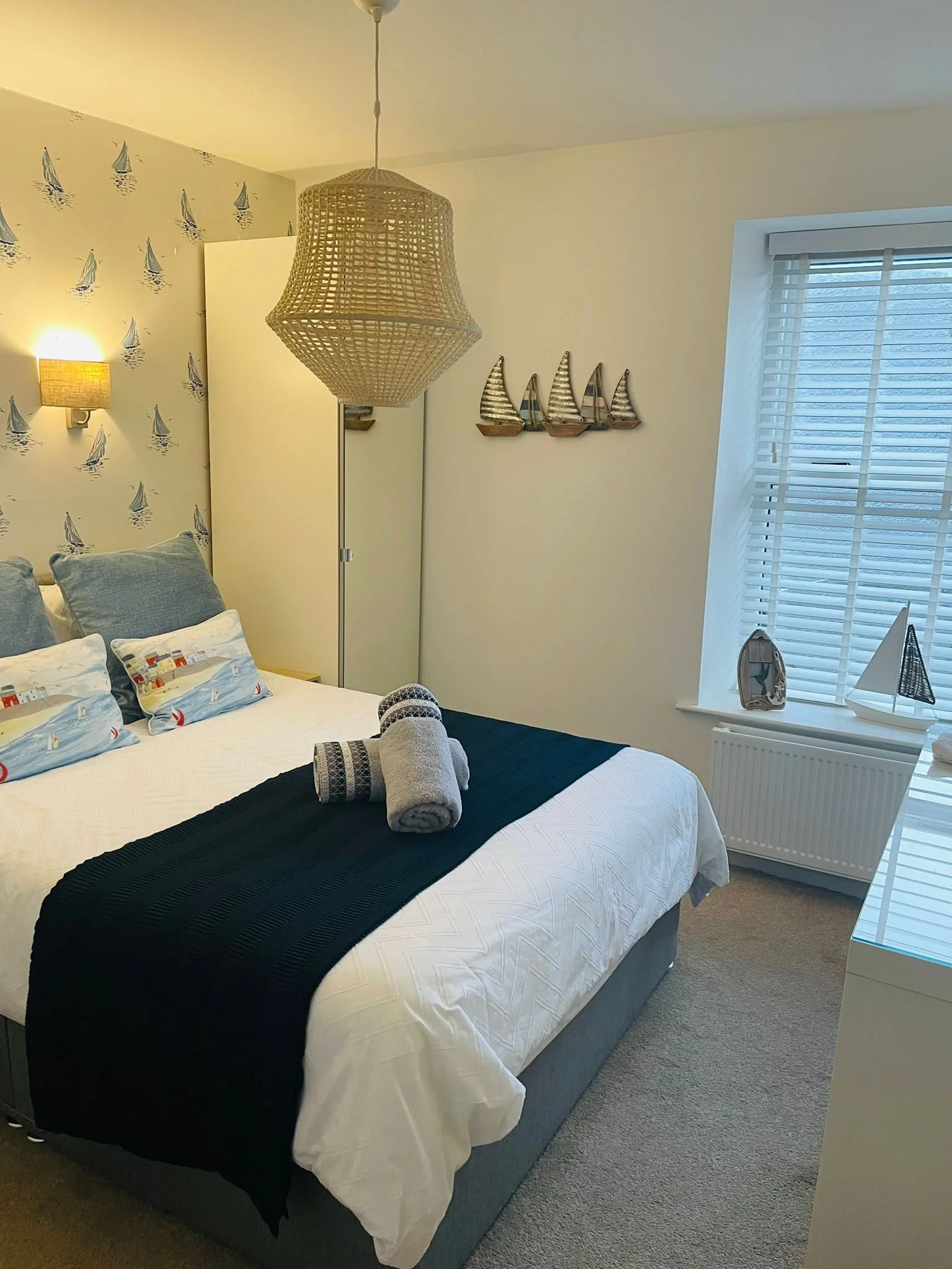 A seaside bedroom with sailboat wall art, nautical decor, and rolled towels on the bed.