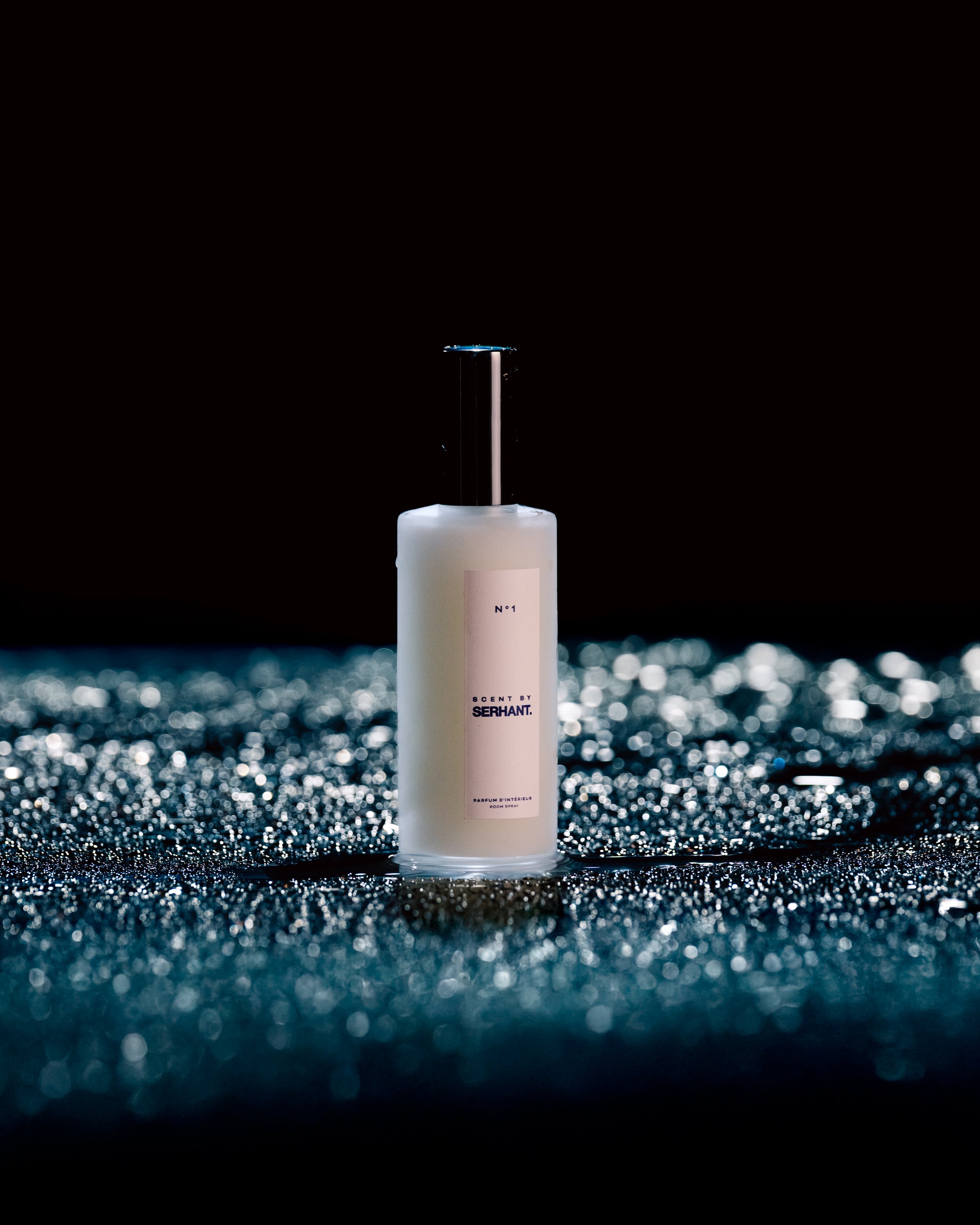 Scent by SERHANT home atmosphere spray — white bottle with black top, styled on a dark glittery surface