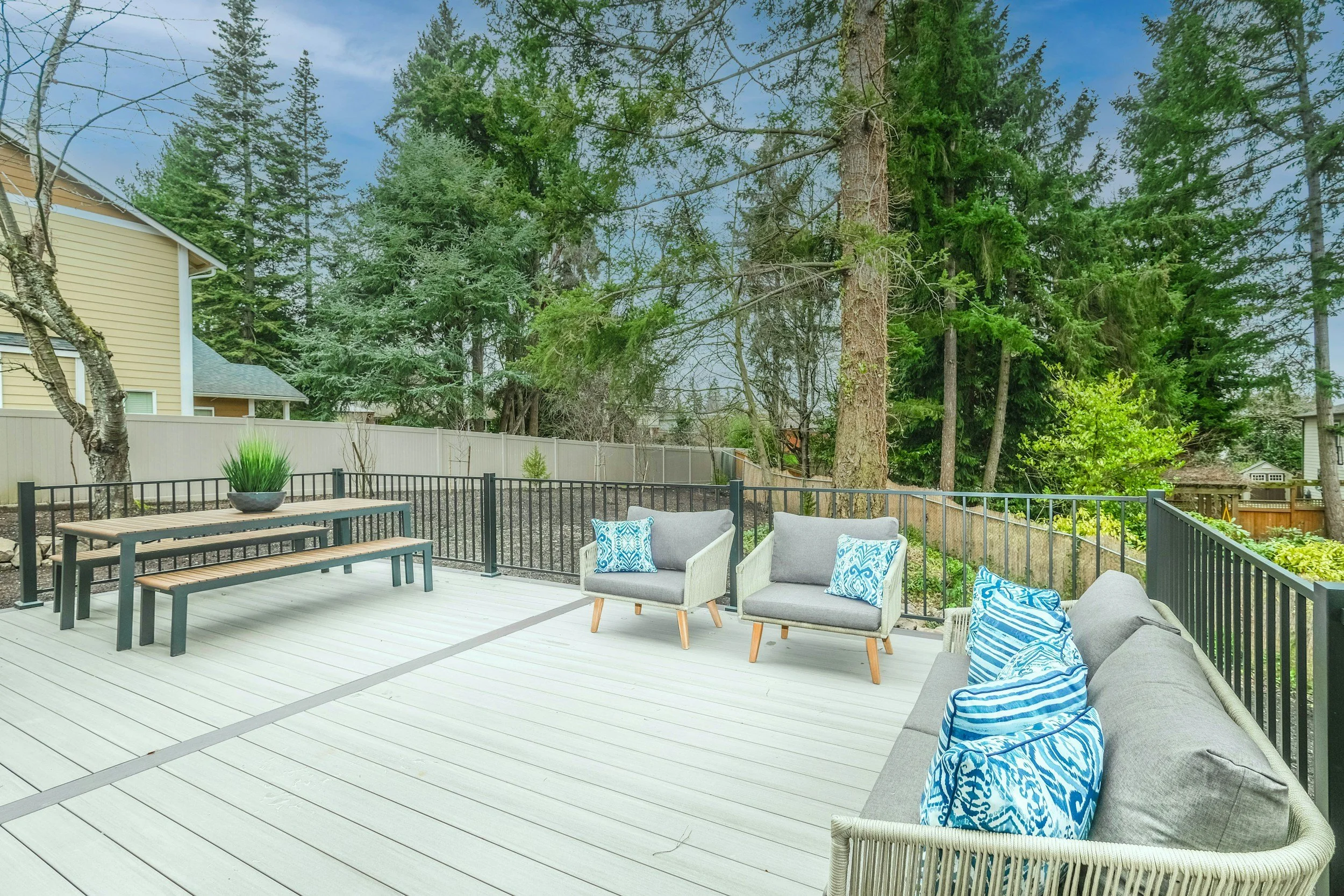 A spacious outdoor deck with seating and a view of tall trees and neighboring houses.