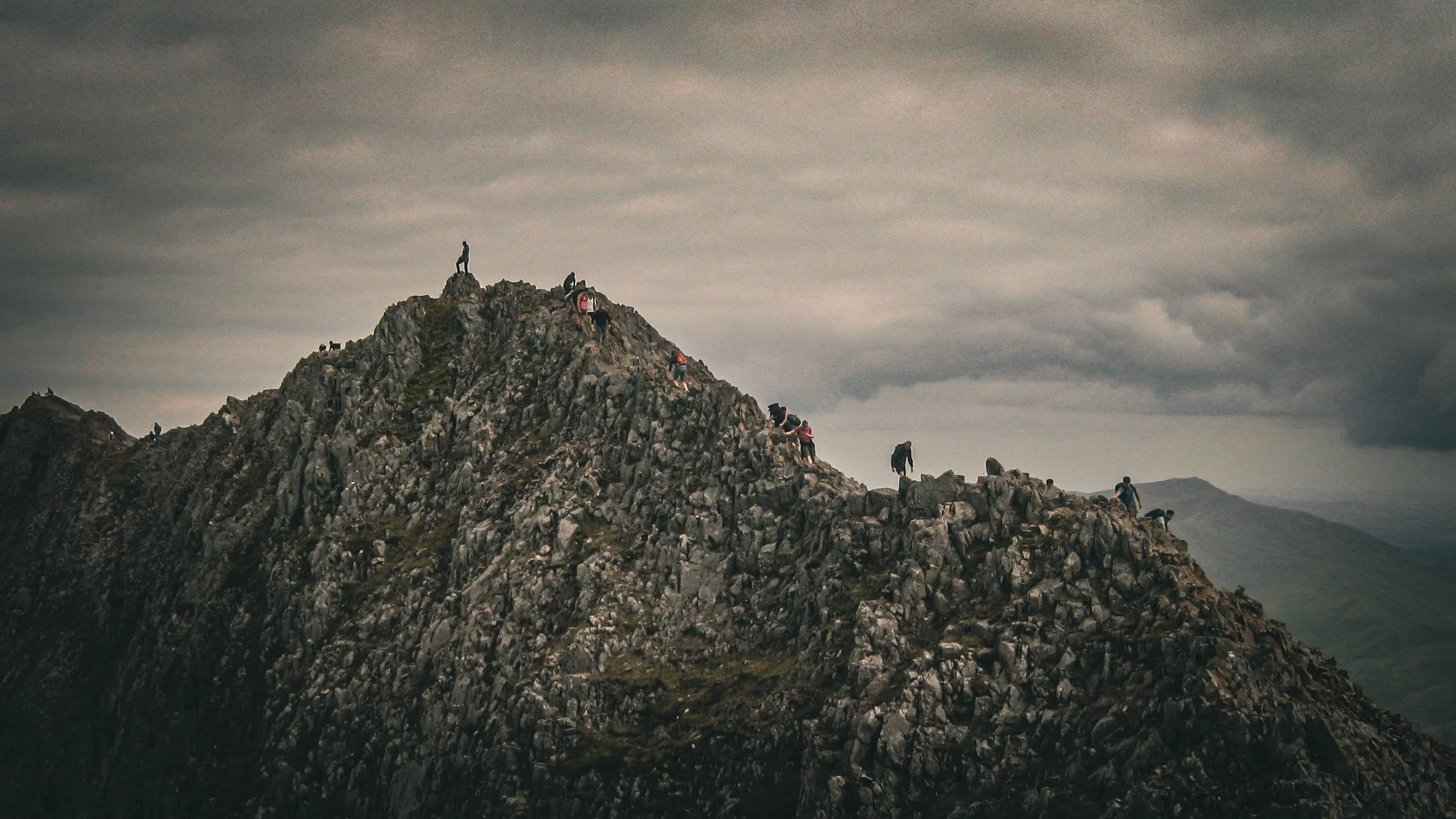 Group of hikers climbing a rocky mountain summit under a cloudy sky.