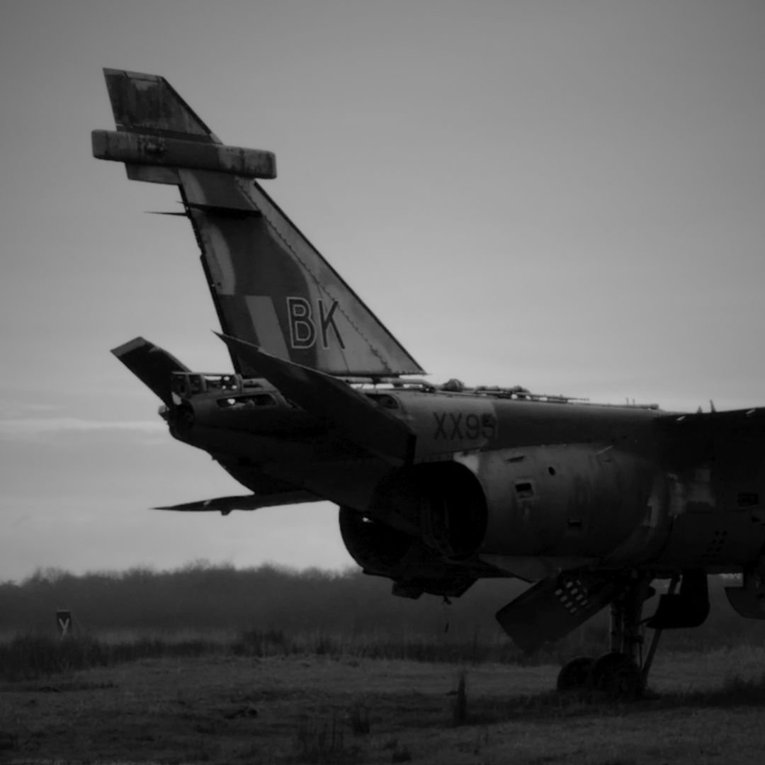 Black and white image of a military fighter jet on the ground, with its tail and part of the fuselage visible.