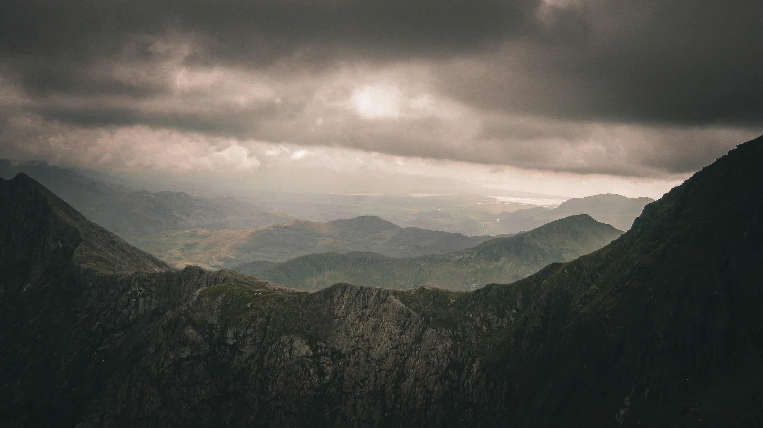 Dark and cloudy mountain landscape with rugged peaks and valleys under a stormy sky.