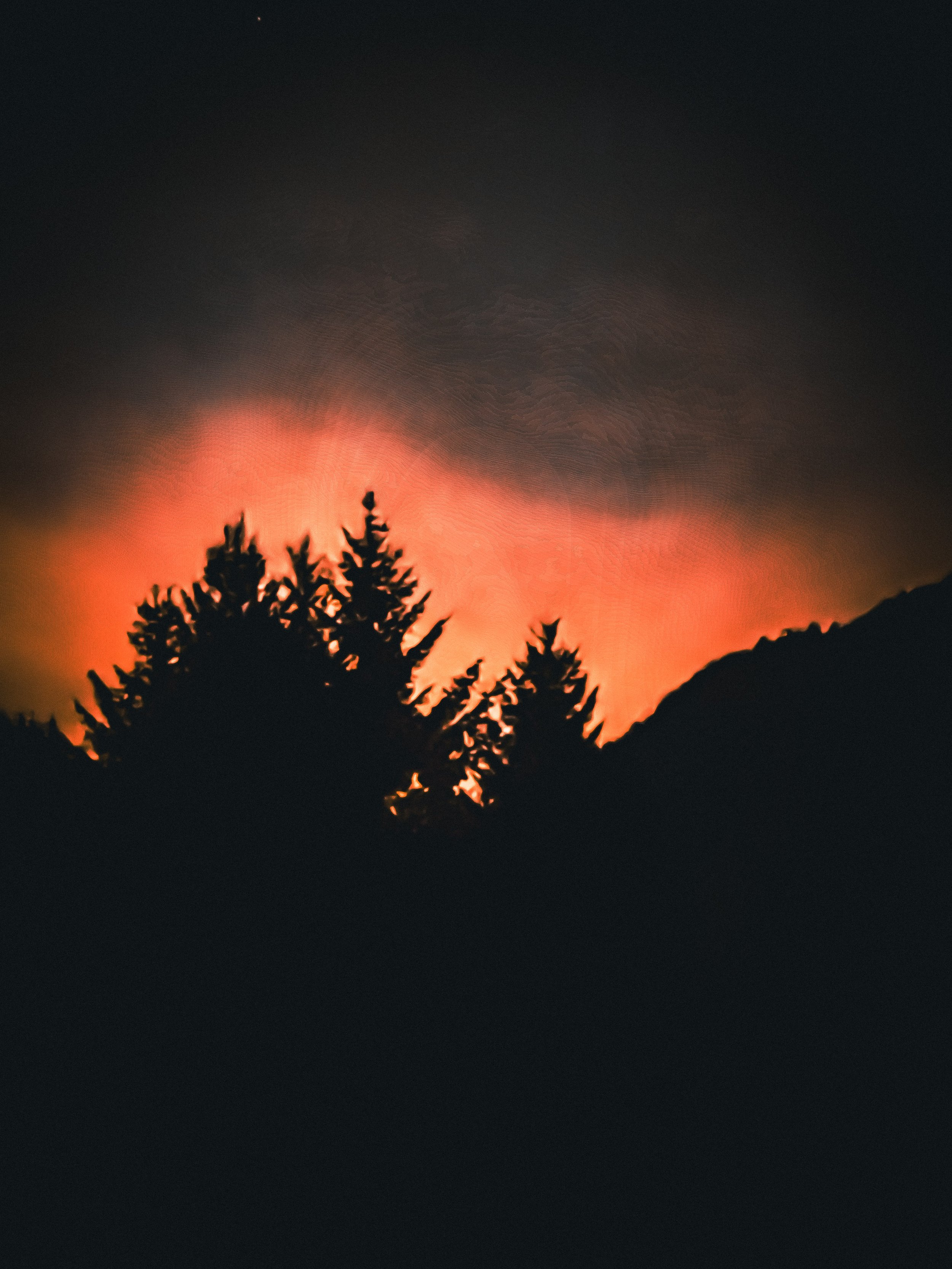 Silhouetted trees against a fiery orange and red sunset sky with dark clouds.