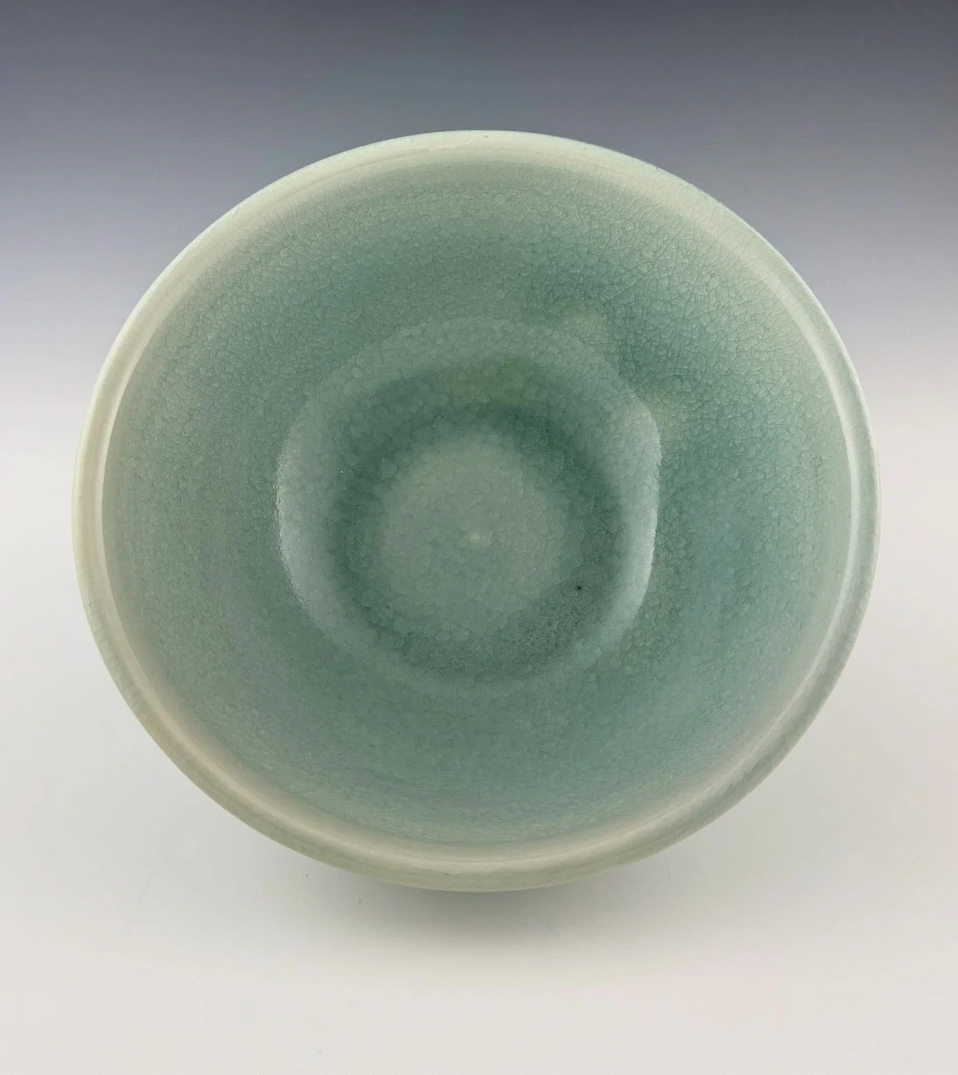 A ceramic bowl with a pale aquamarine glaze, viewed from above, showing its interior surface with a crackled texture.