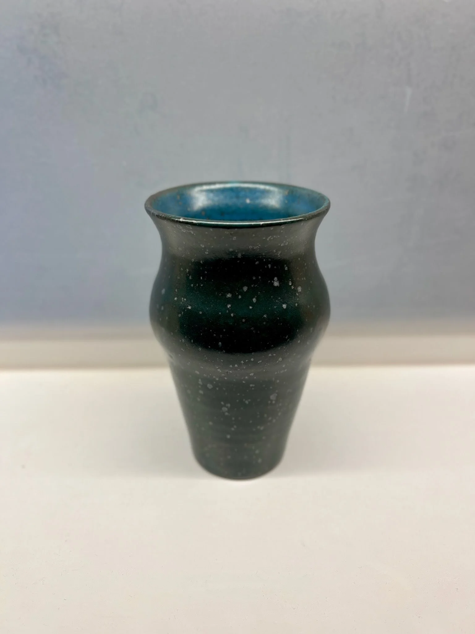 A black ceramic vase with a blue interior, on a plain white surface against a gray background.