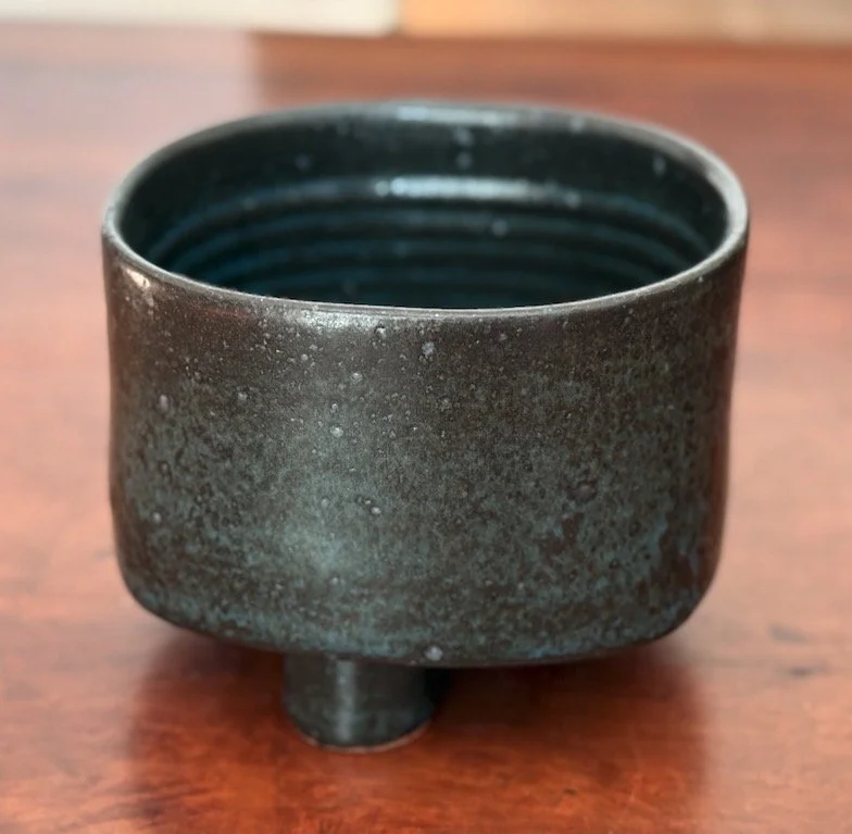 A small, blue-black ceramic container with a three cylindrical feet, placed on a wooden surface.