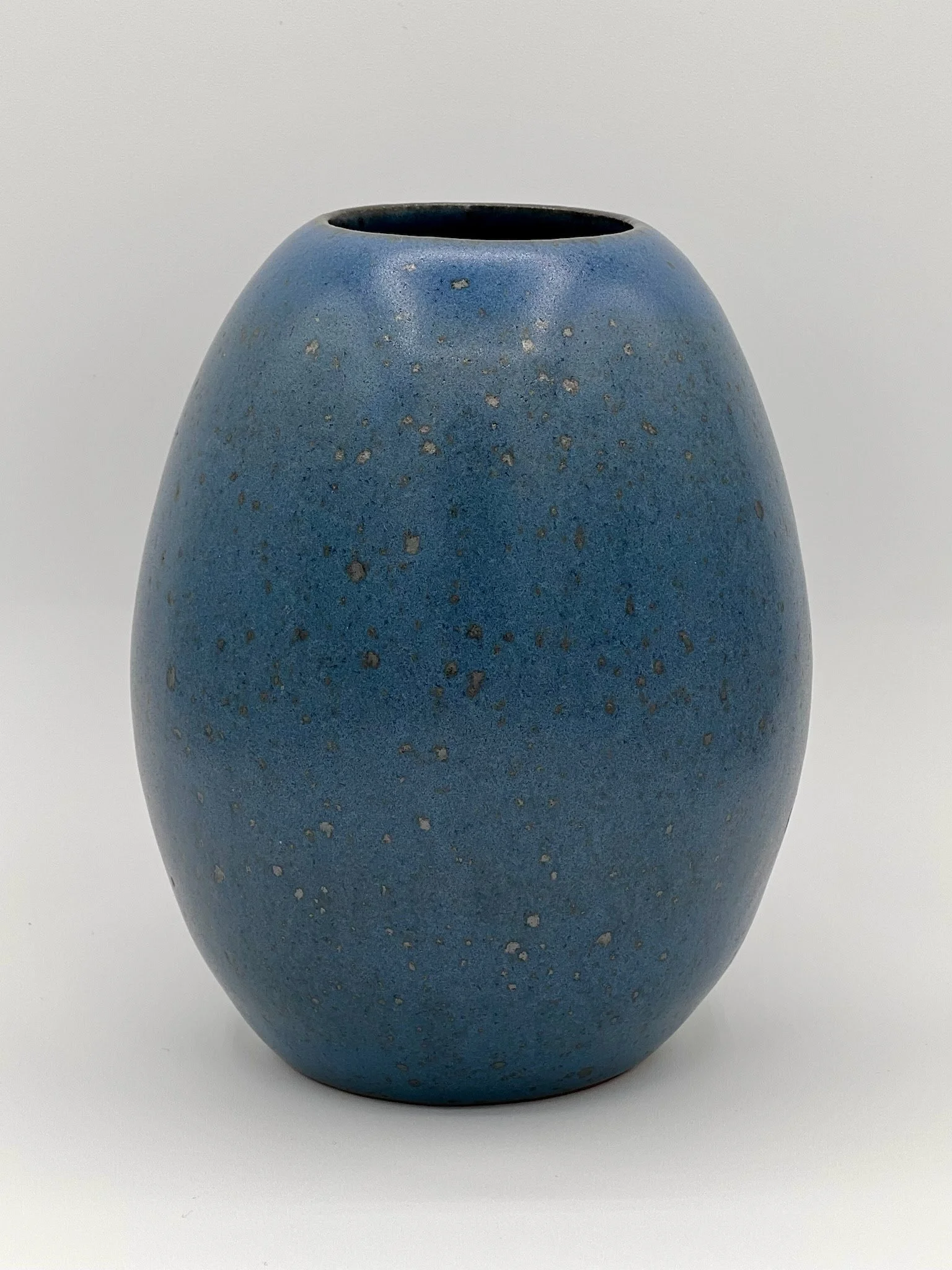 A blue ceramic vase with a rounded, slightly elongated egg-like shape, set against a plain background.