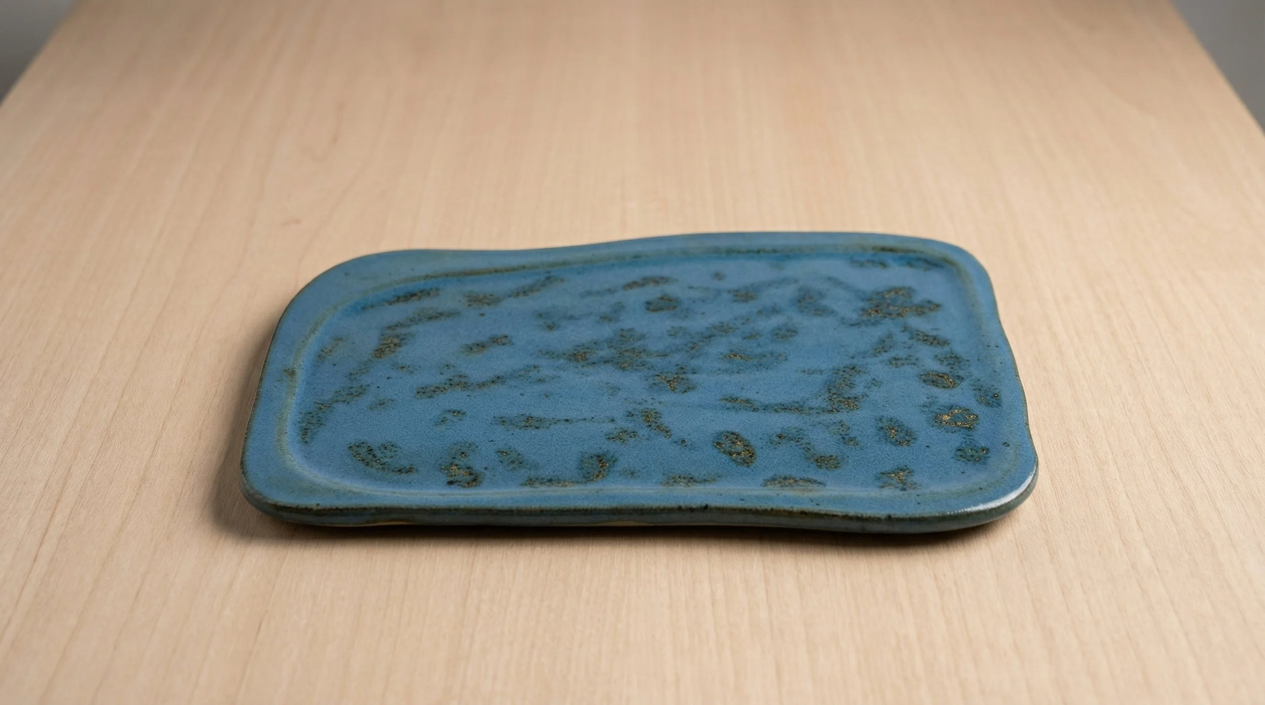 A rectangular ceramic platter with a blue glaze with gold mottling, resting on a wooden surface.